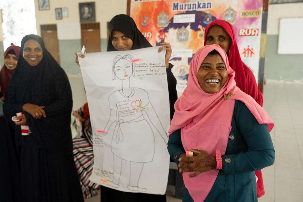 Fünf Frauen blicken lachend in die Kamera, eine hält ein Plakat mit einer gezeichneten Frau hoch (Quelle: Christian Nusch)