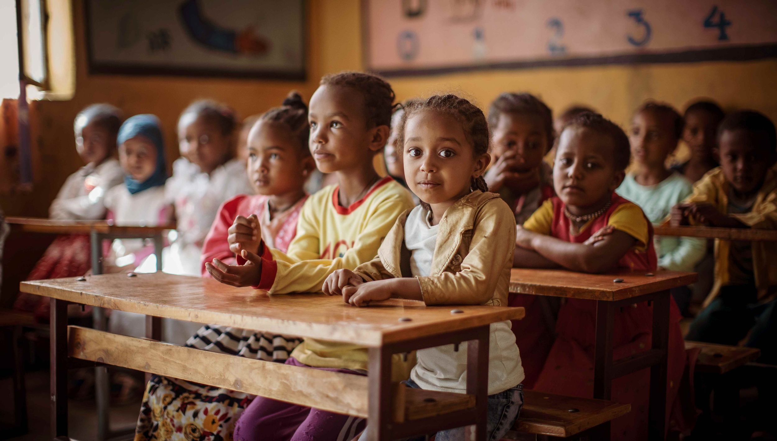 Schulkinder hinter Holzpulten, drei Mädchen im Vordergrund sind aufmerksam oder lächeln  (Bildquelle: Jakob Studnar)