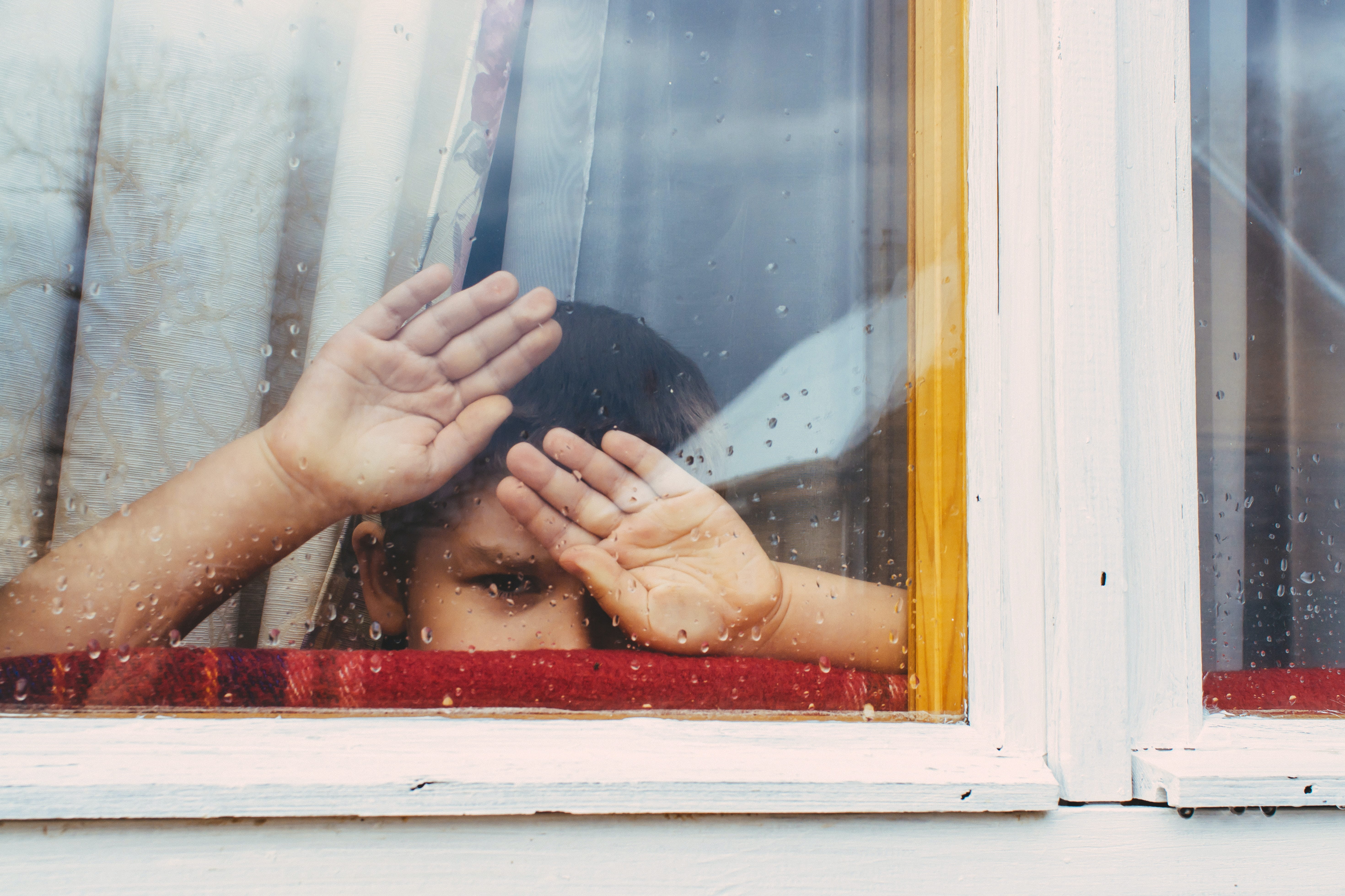 Junge schaut traurig durch eine Fensterscheibe 