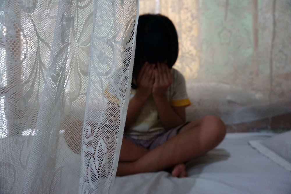 Ein Mädchen sitzt mit vor dem Gesicht verschränkten Händen auf einem Bett. (Quelle: Christiane Dase)