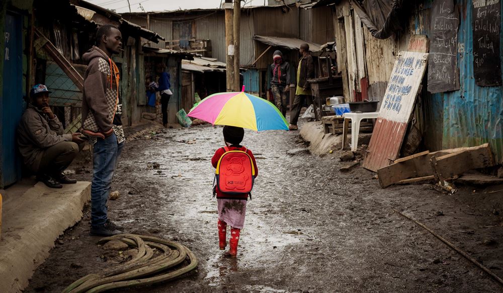 Ein Junge läuft mit einem bunten Regenschirm durch einen Slum in Kenias Hauptstadt Nairobi. (Quelle: Lars Heidrich)