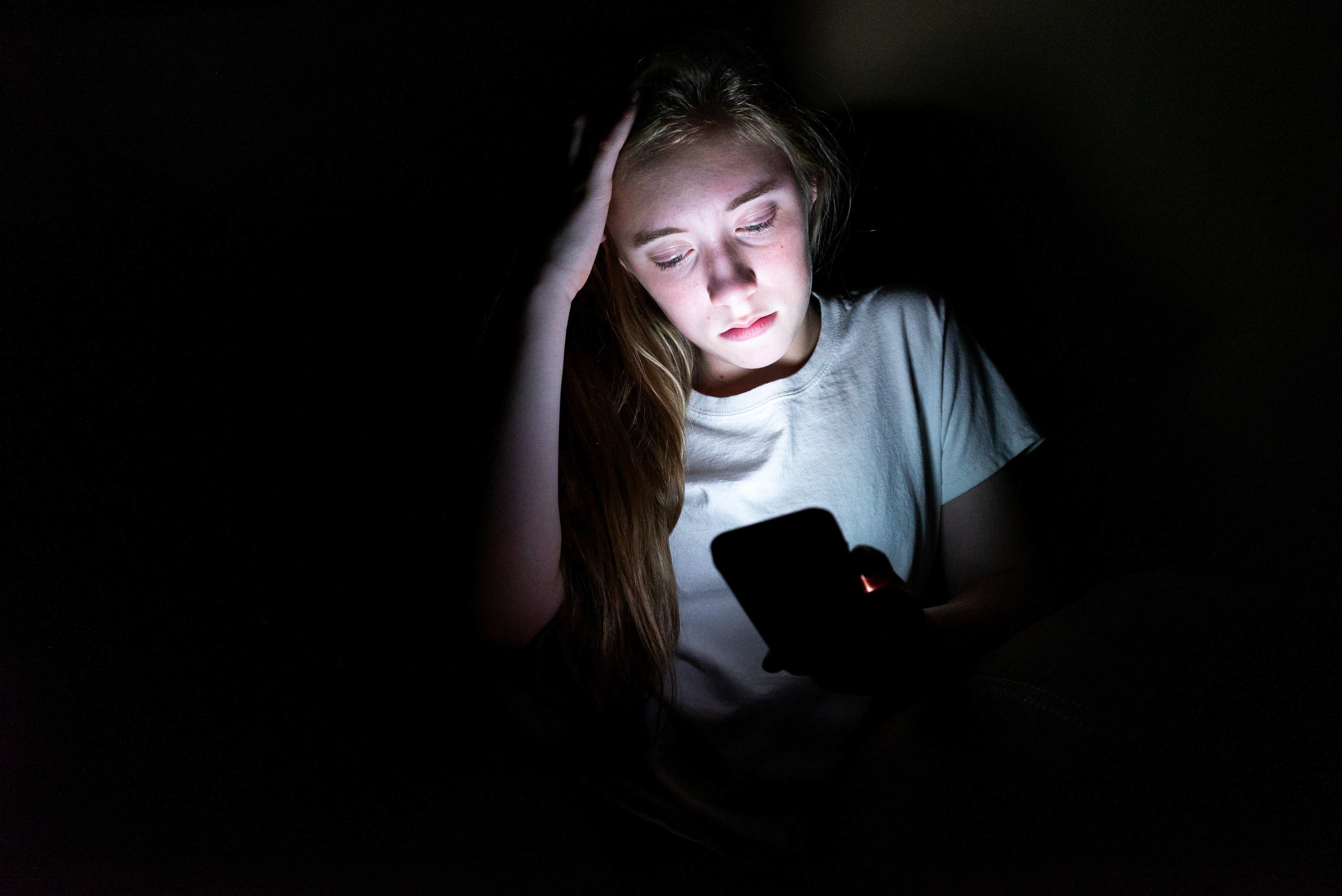 Mädchen schaut im Dunkeln auf ihr Smartphone (Quelle: Brian/Adobe Stock)