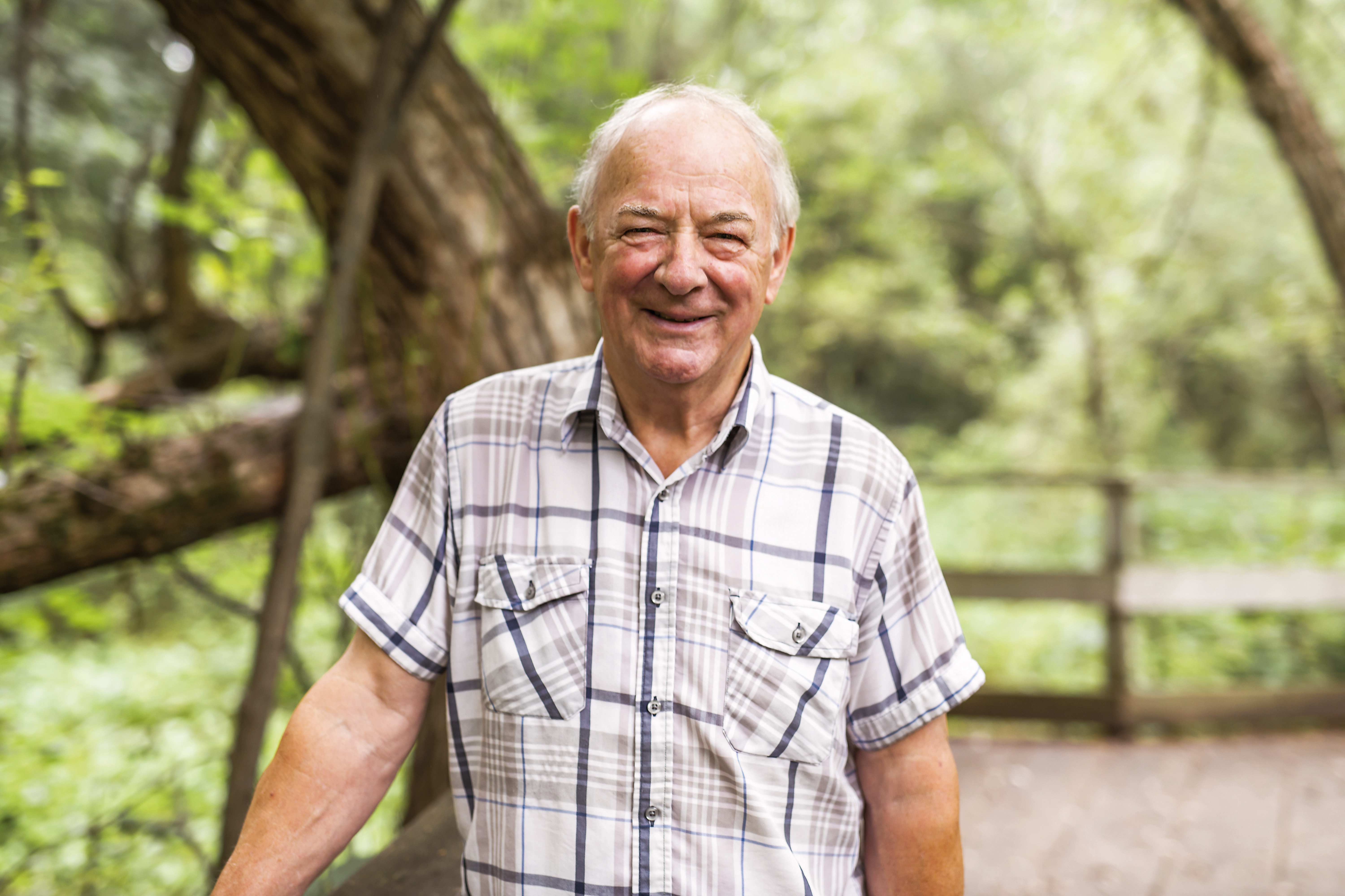 Ein älterer Mann in kariertem Hemd lächelt.
