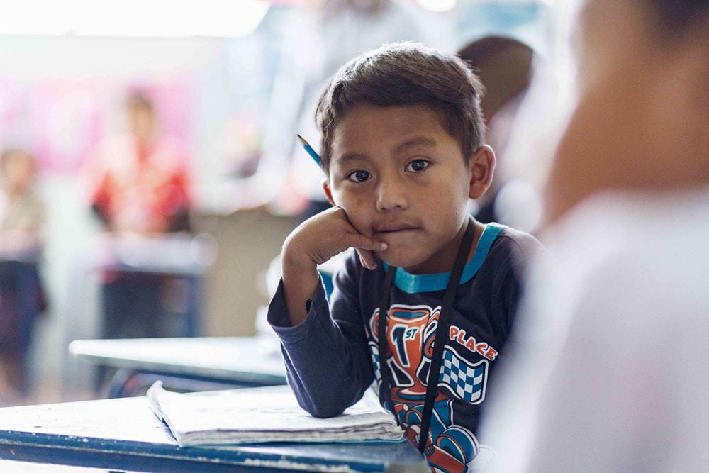 Ein Junge aus Guatemala sitzt in der Schule und schaut in die Kamera. (Quelle: Jakob Studnar)