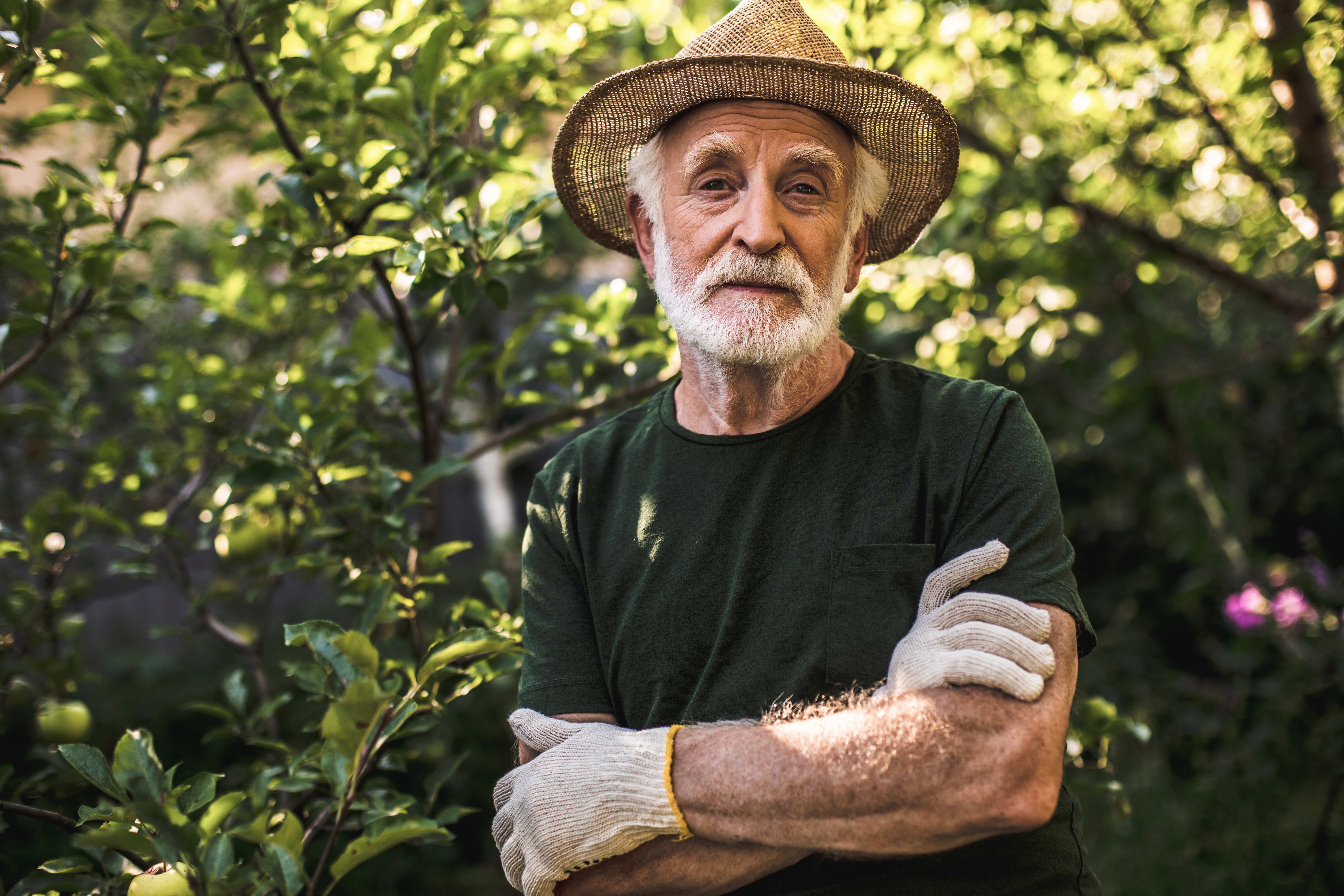 Ein Mann mit Strohhut steht vor grünen Büschen.