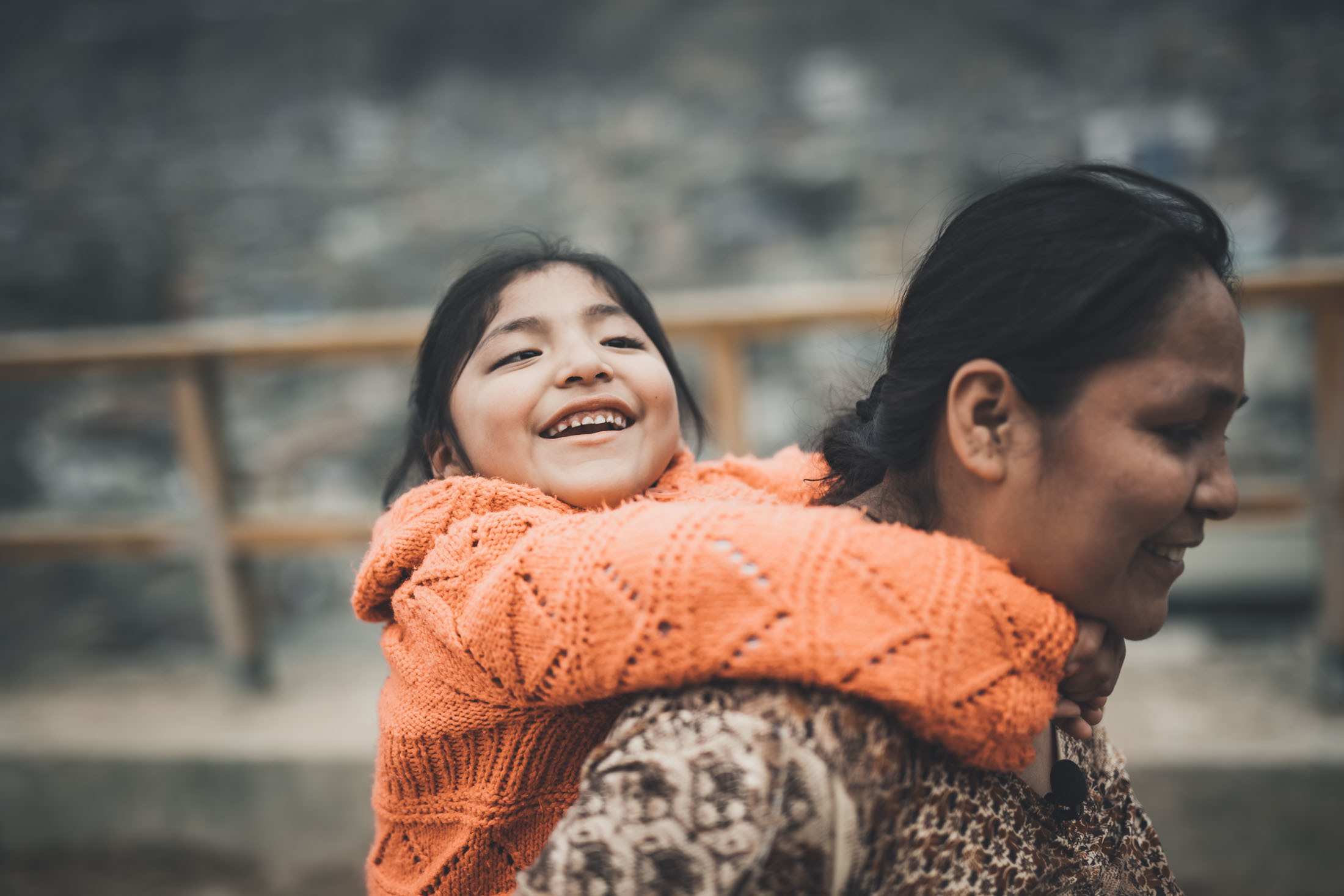 Eine Mutter aus Peru trägt ihre lachende Tochter auf dem Rücken. (Quelle: Jakob Studnar)