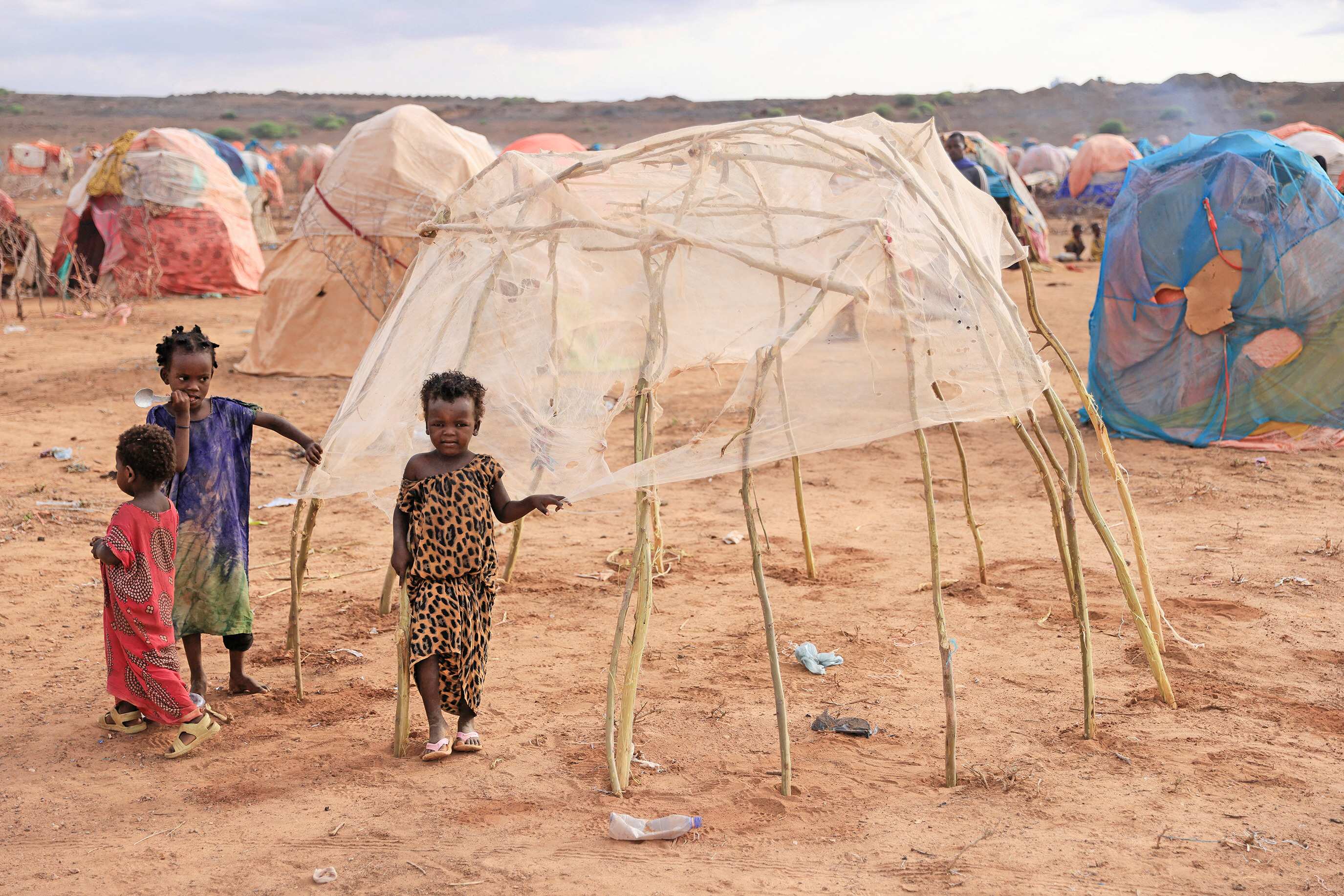 Children stand next to a makeshift shelter at the Higlo camp for people displaced by drought