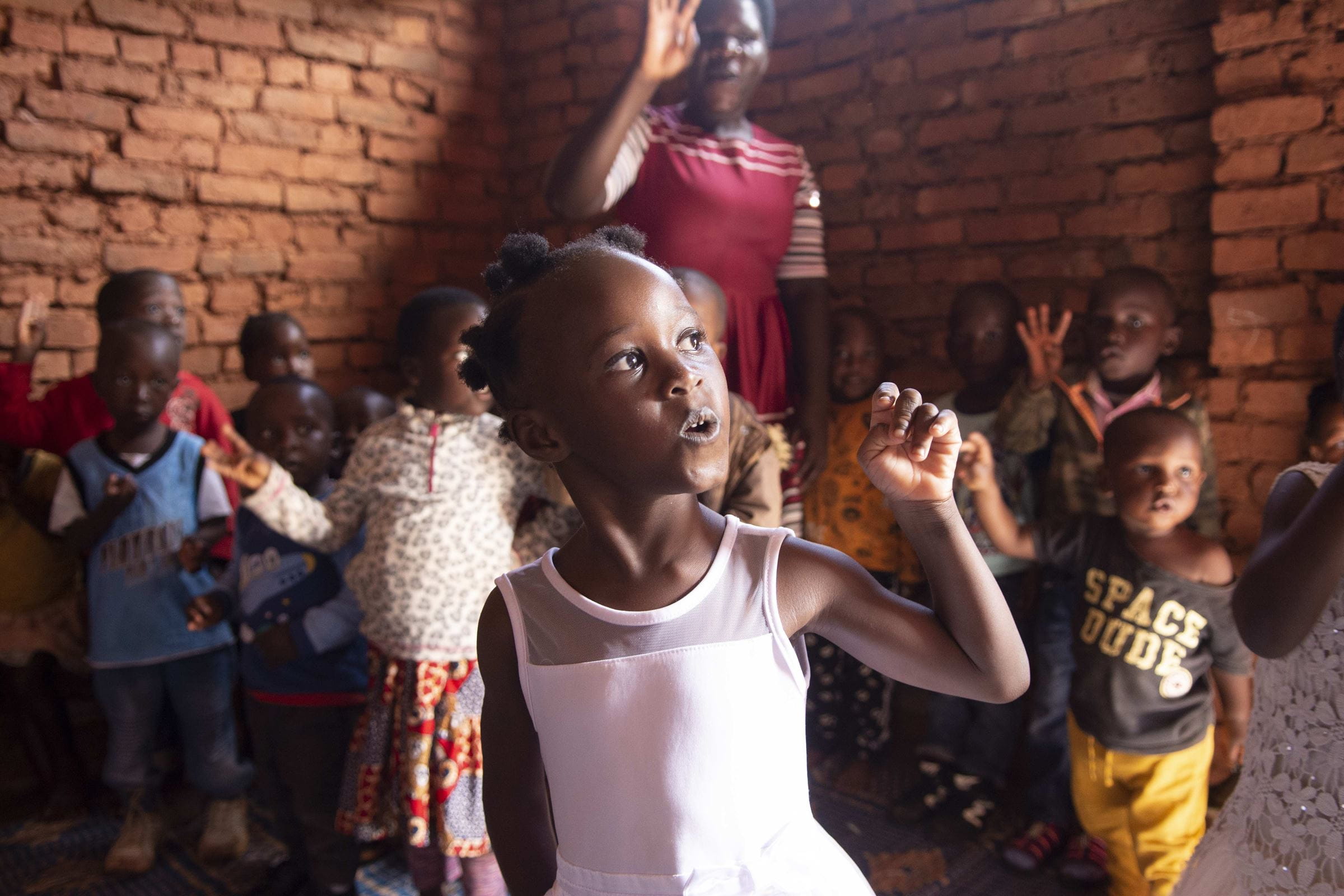 Ein Mädchen mit zerebraler Kinderlähmung steht in Malawi in ihrem Kindergarten. Im Hintergrund sind andere Kindergartenkinder und ihre Lehrerin (Quelle: Christian Nusch)