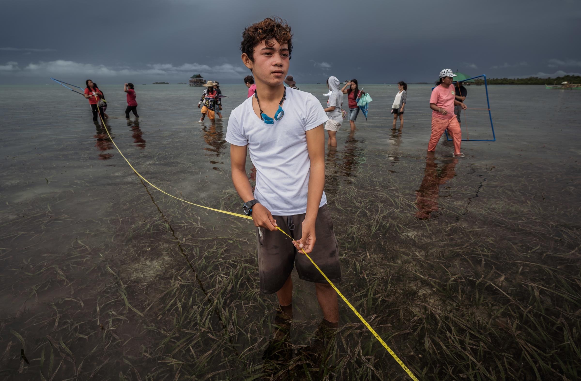 Ein Junge steht im Meer und hält ein Maßband um das Seegras im Küstenbereich zu vermessen. (Foto: Jakob Studnar)