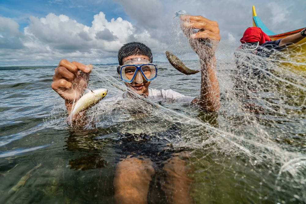 Der Fischerjunge Rico hält im Wasser ein Netz mit zwei Fischen in die Kamera (Quelle: Jakob Studnar)