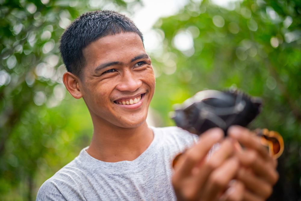Der Fischerjunge Rico hält eine Muschel in die Kamera (Quelle: Jakob Studnar)
