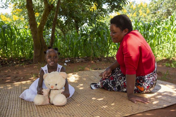 Ein Mädchen aus Malawi mit Teddybär im Arm sitzt mit ihrer Mutter auf einer Strohmatte. (Quelle: Christian Nusch)