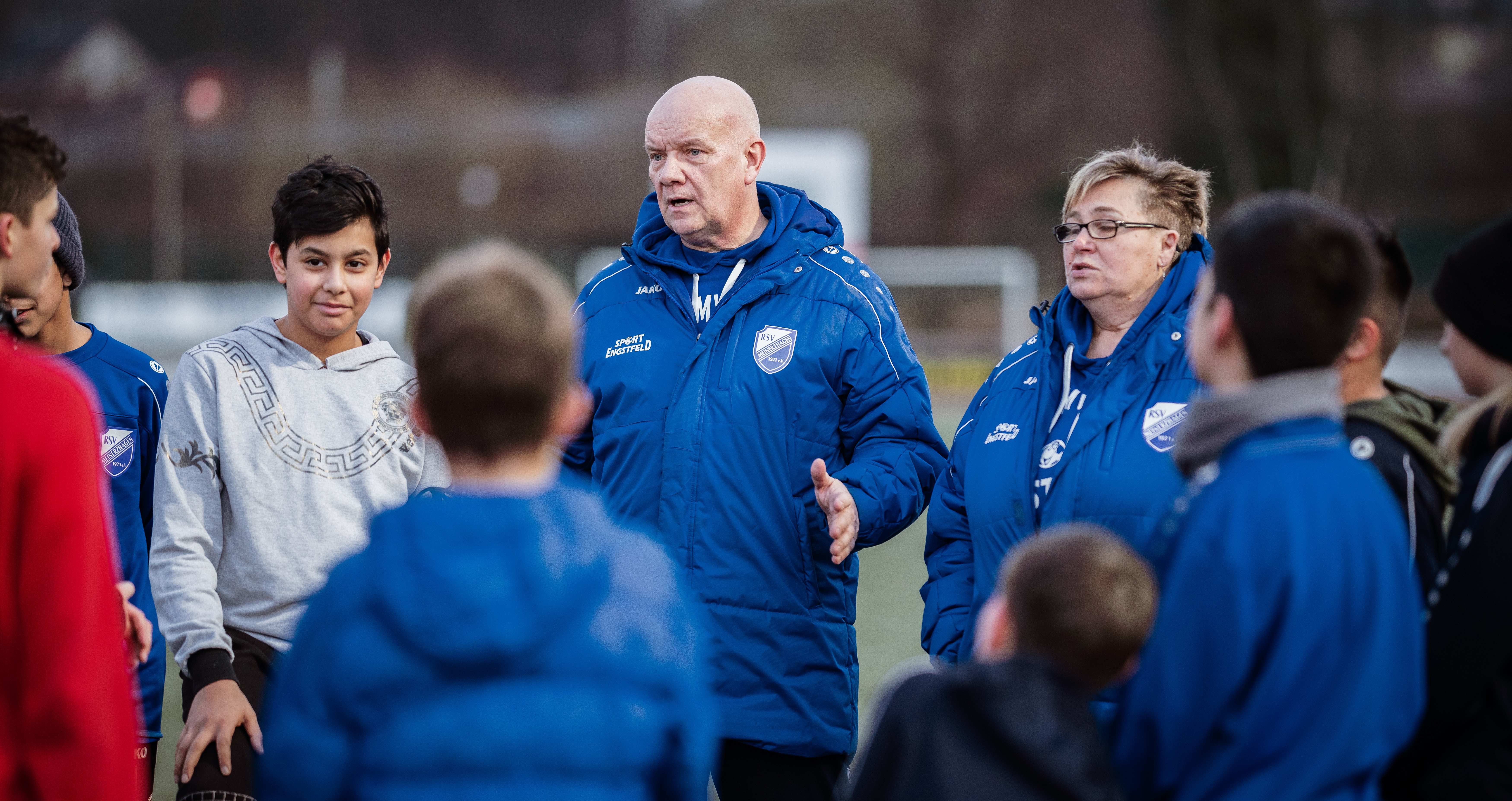 Ein Fußballtrainer spricht mit Kindern und Jugendlichen auf dem Fußballplatz. Foto: Jakob Studnar