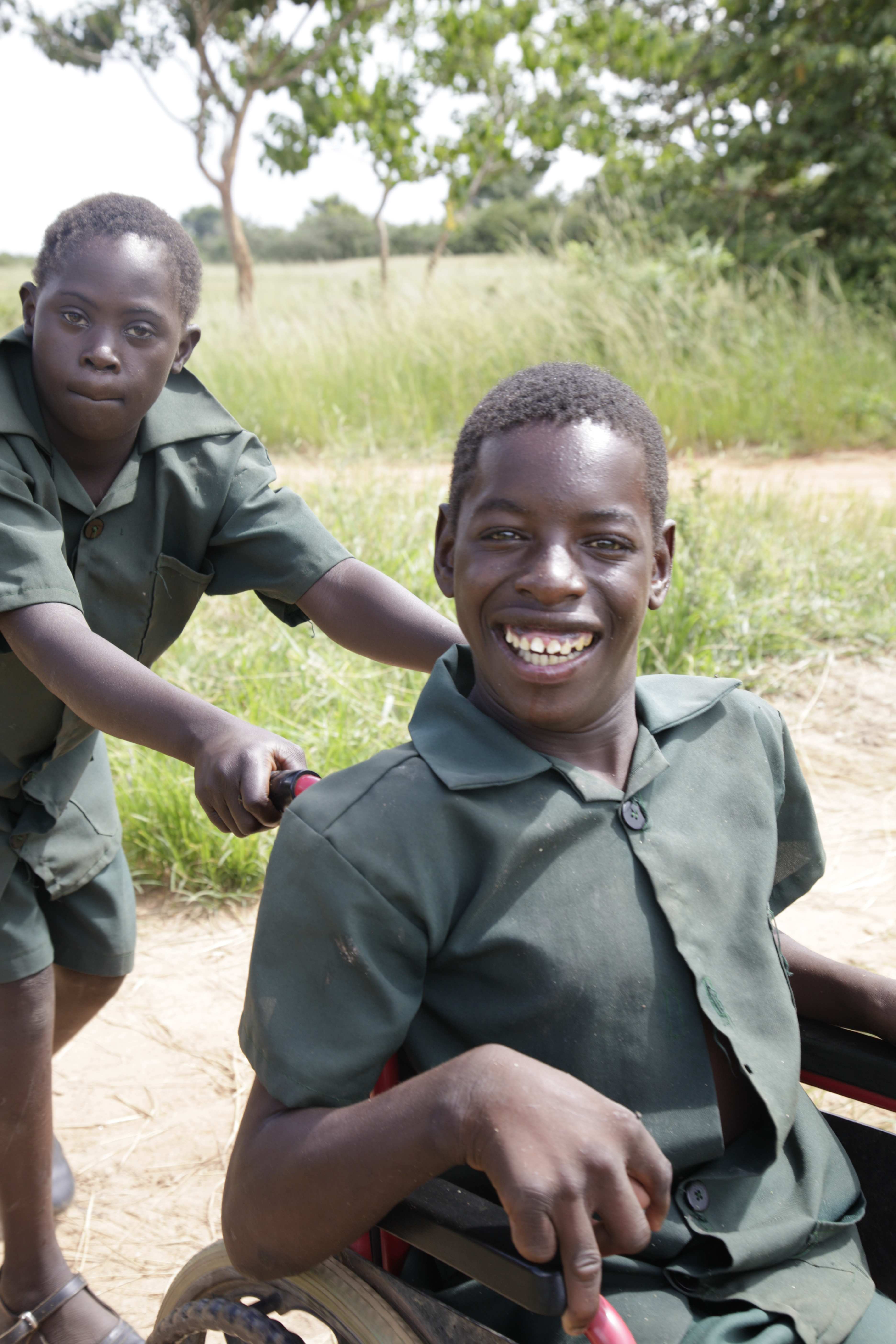 Junge aus Sambia schiebt anderen Jungen im Rollstuhl