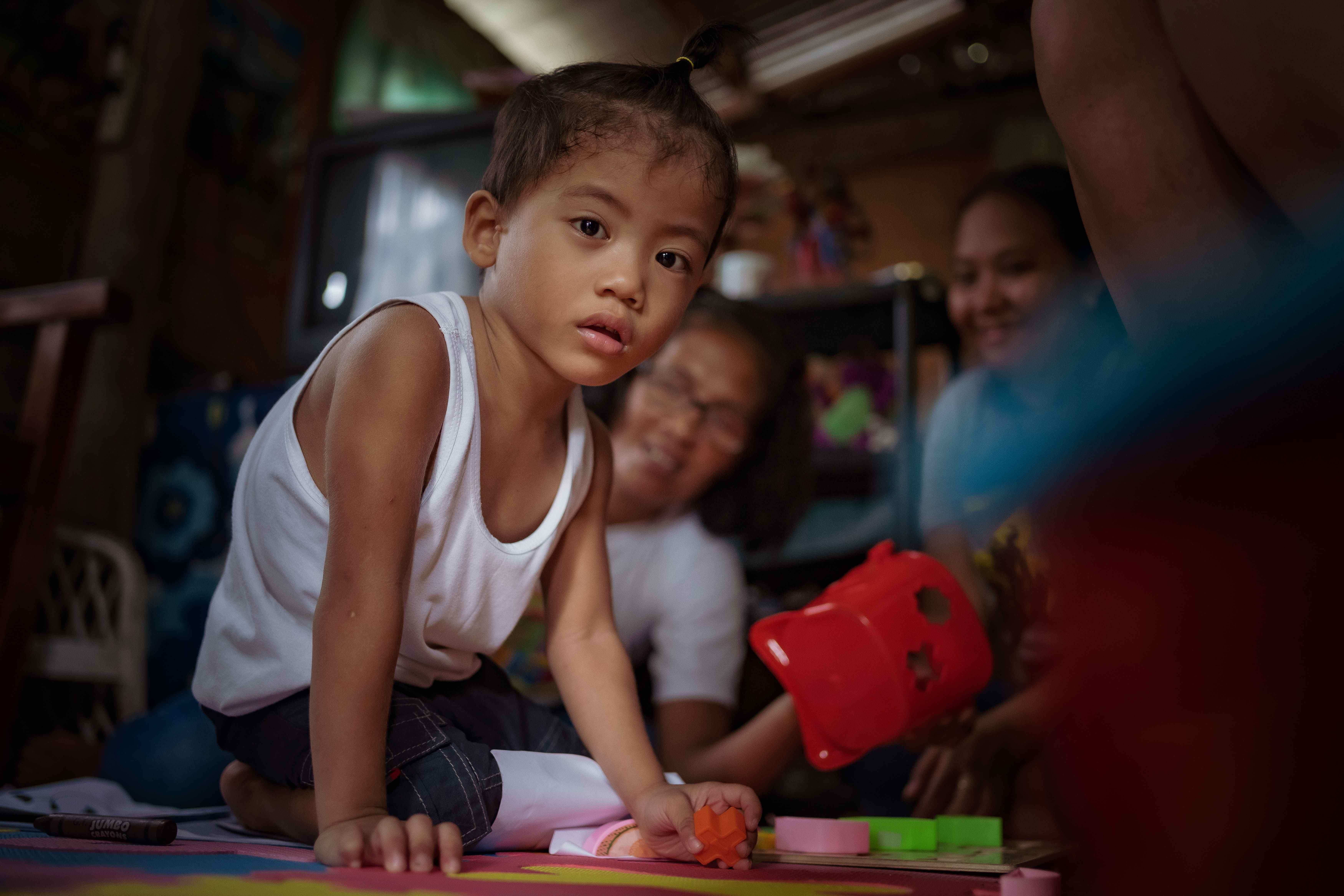 Ein kleiner Junge krabbelt auf dem Boden in einer Hütte, im Hintergrund sitzen zwei Frauen (Quelle: Jakob Studnar)