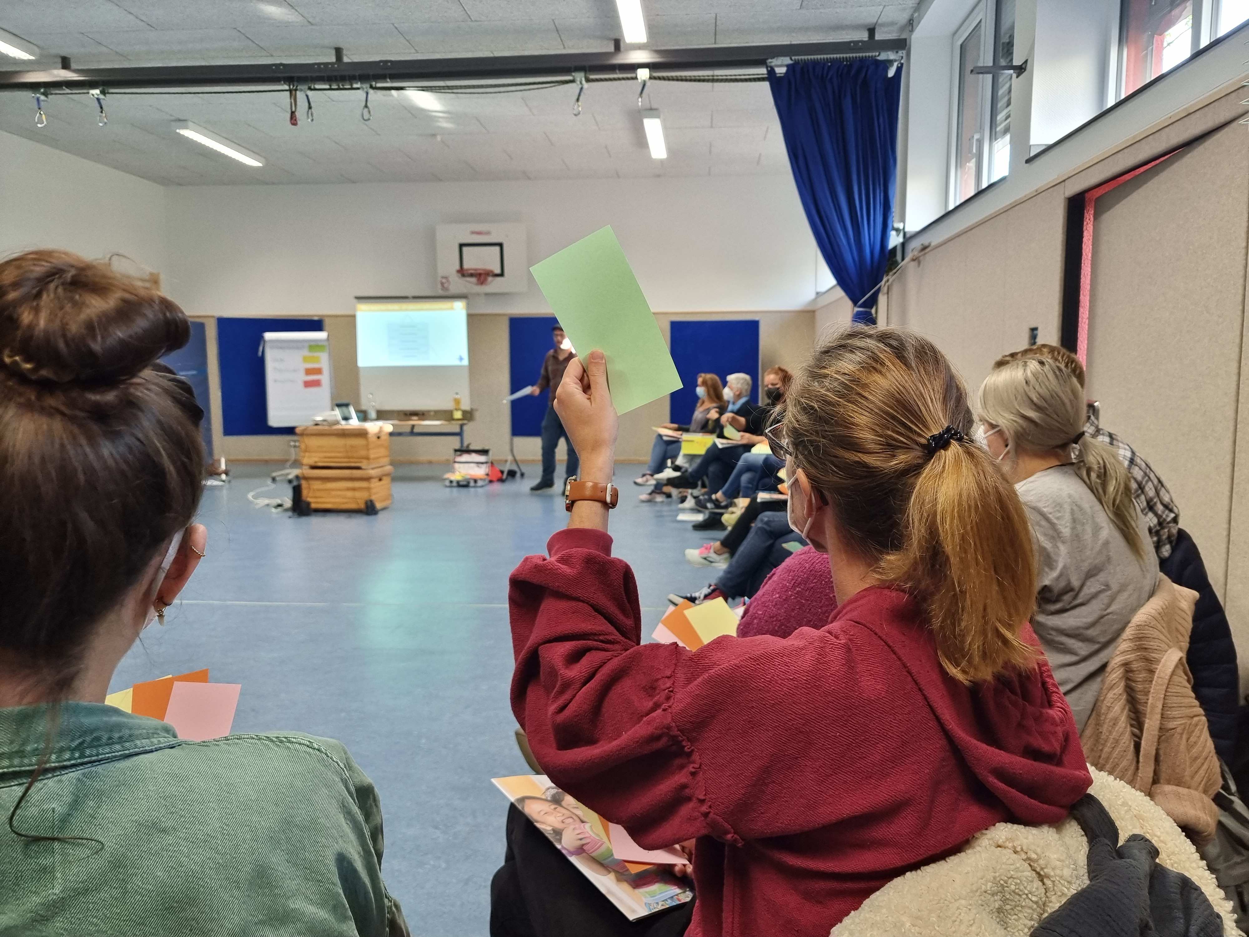 Teilnehmende einer Inhouse Schulung sitzen zusammen im Kreis in einer Sporthalle. Foto: Kindernothilfe