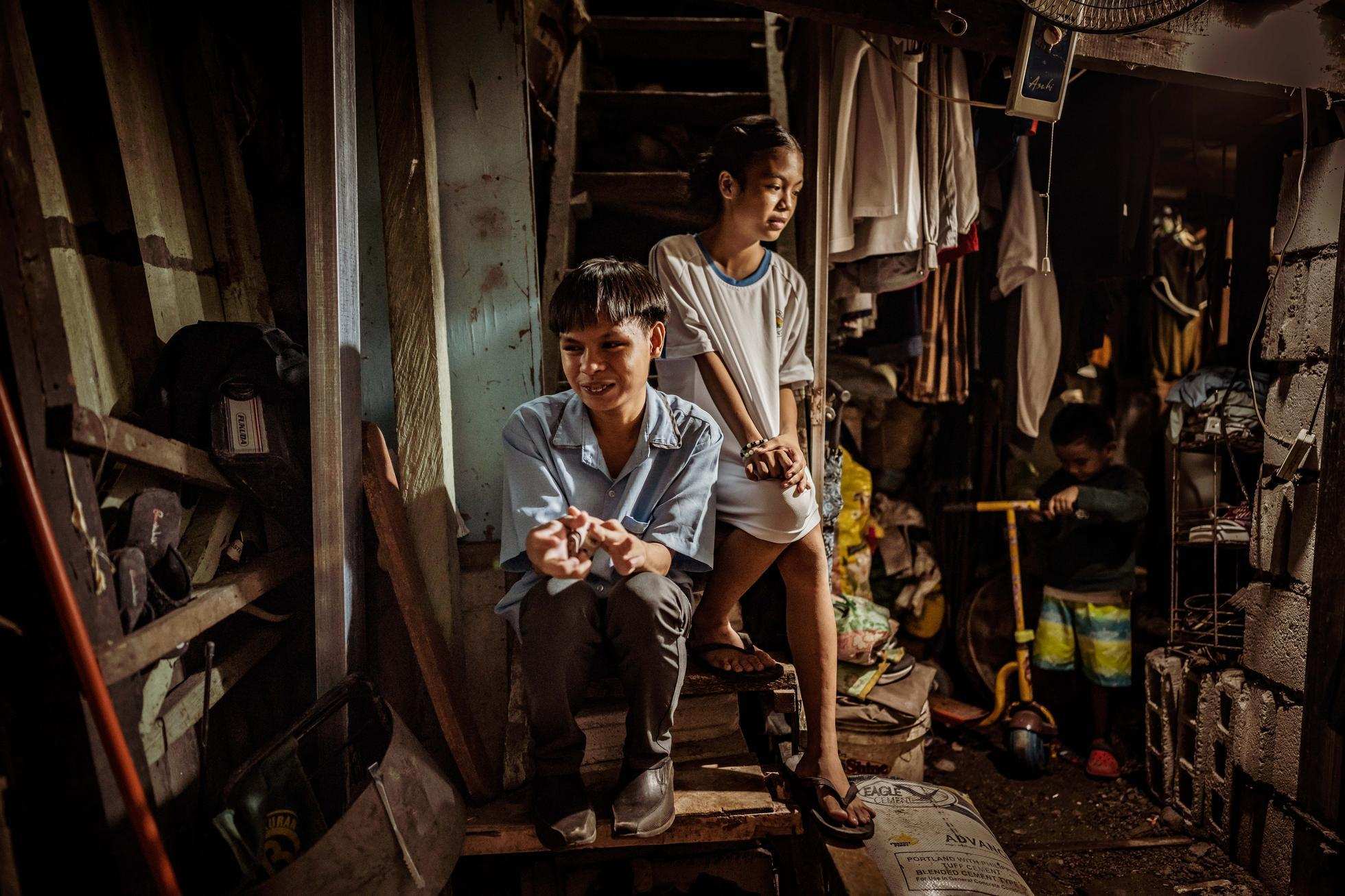 Ein Junge und ein Mädchen sitzen auf den Treppenstufen ihrer vollgestellten, engen Wohnung in einem Slum in Manila. (Quelle: Jakob Studnar)