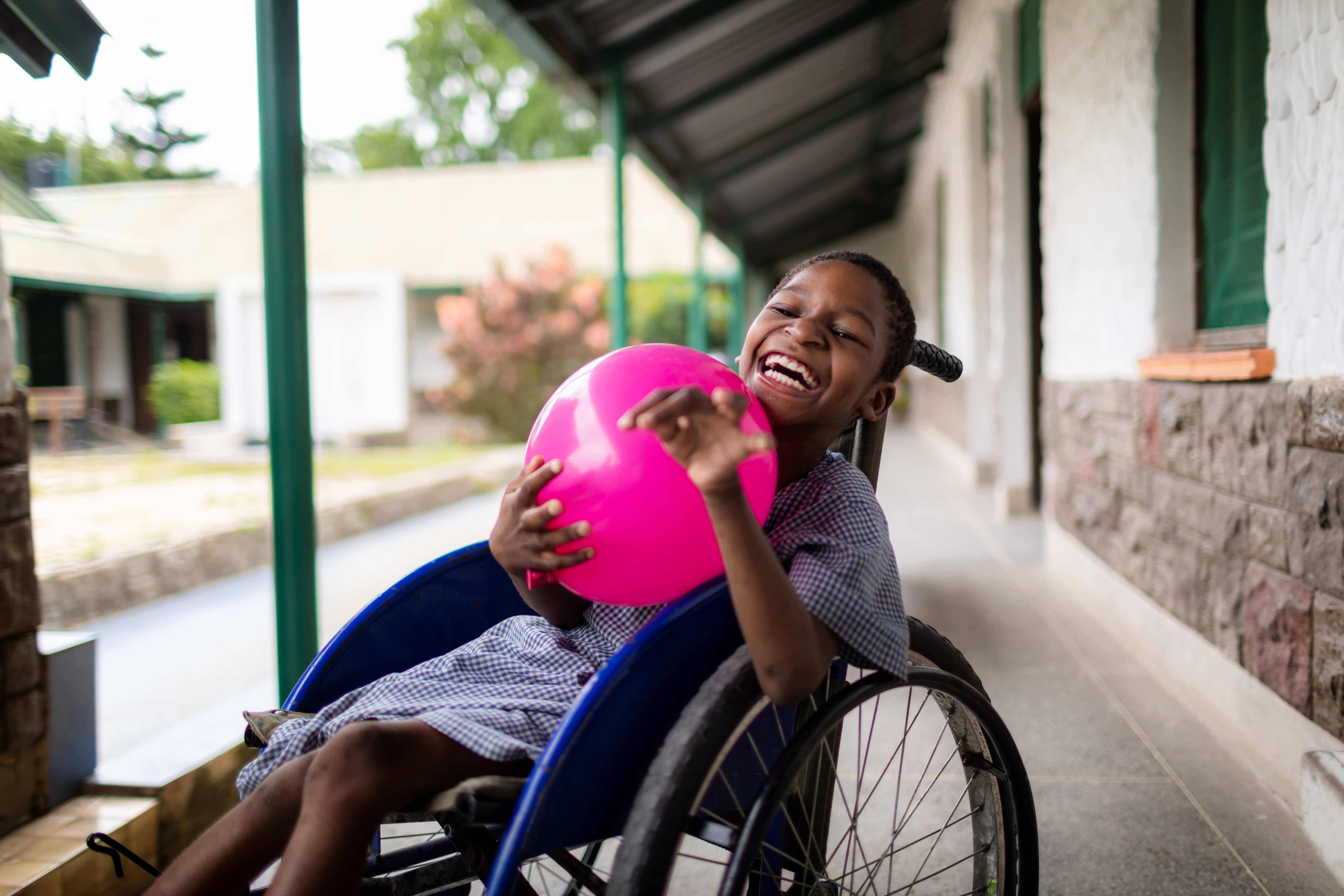 Junge im Rollstuhl hält einen Ball und lacht. (Quelle: Lars Heidrich)
