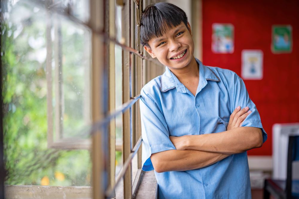 Mic steht ans Fenster gelehnt in einem Klassenzimmer und lacht (Foto Jakob Studnar) Platzhalterbild