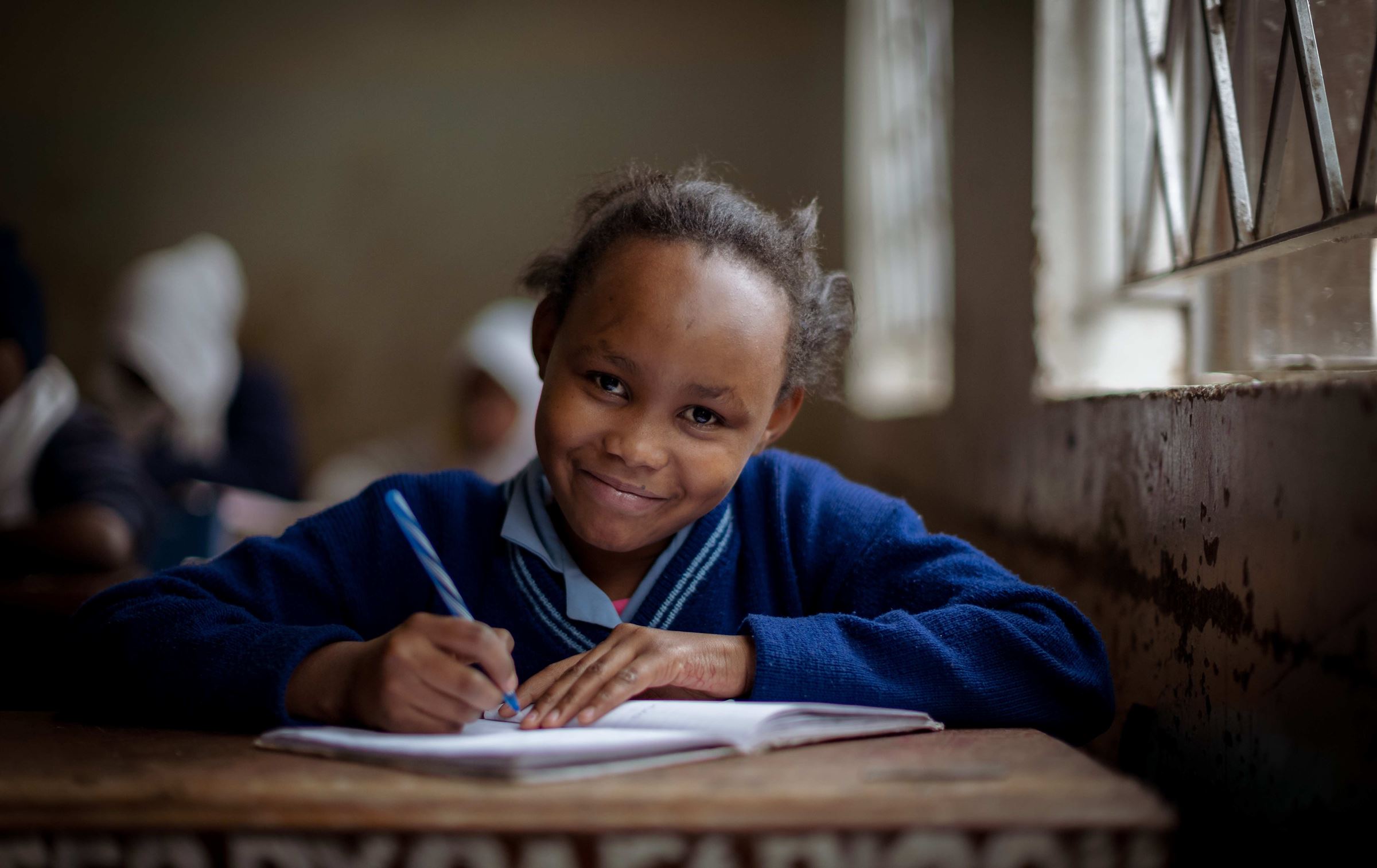 Ein Mädchen sitzt in der Schule und lächelt in die Kamera. (Quelle: Lars Heidrich)
