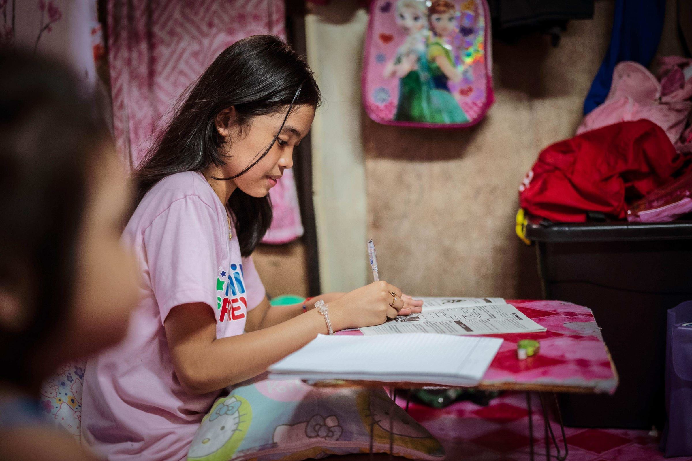 Ein Mädchen hockt auf dem Boden in der Hütte ihrer Eltern in einem Slum in Manila und macht ihre Hausaufgaben (Quelle: Jakob Studnar)