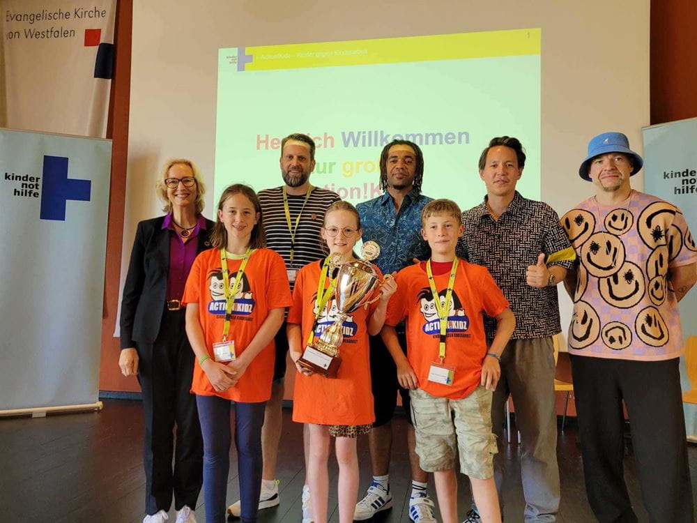 Hinten: Vorstandsvorsitzende der Kindernothilfe, Katrin Weidemann, Dirk Lepping, Unterstufenkoordinator am Ev. Gymnasium Lippstadt, Culcha Candela. Vorne: Schülerinnen und Schüler der Gewinnerschule (Quelle: Kindernothilfe). Hinten: Vorstandsvorsitzende der Kindernothilfe, Katrin Weidemann, Dirk Lepping, Unterstufenkoordinator am Ev. Gymnasium Lippstadt, Culcha Candela. Vorne: Schülerinnen und Schüler der Gewinnerschule (Quelle: Kindernothilfe).