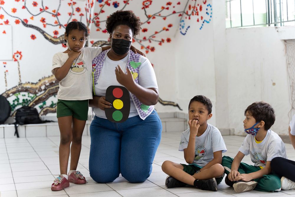 Projektleiterin Viviane Silva kniet mit einer aufgemalten Ampel in der Hand zwischen den Kindern (Quelle: Christian Nusch)