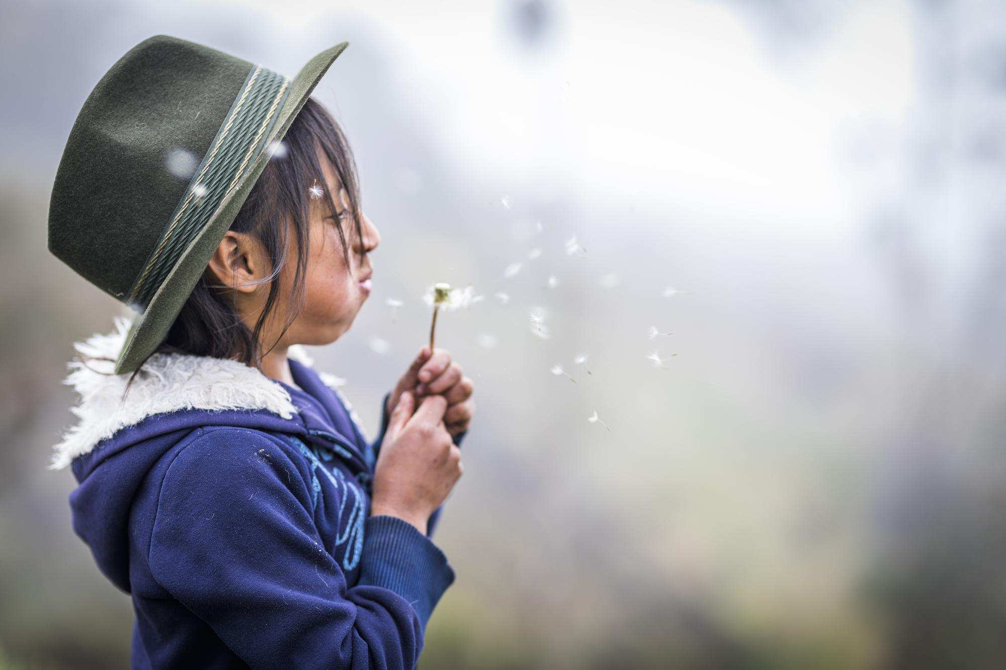 Mädchen aus Peru pustet gegen eine Pusteblume (Quelle: Kindernothilfe)