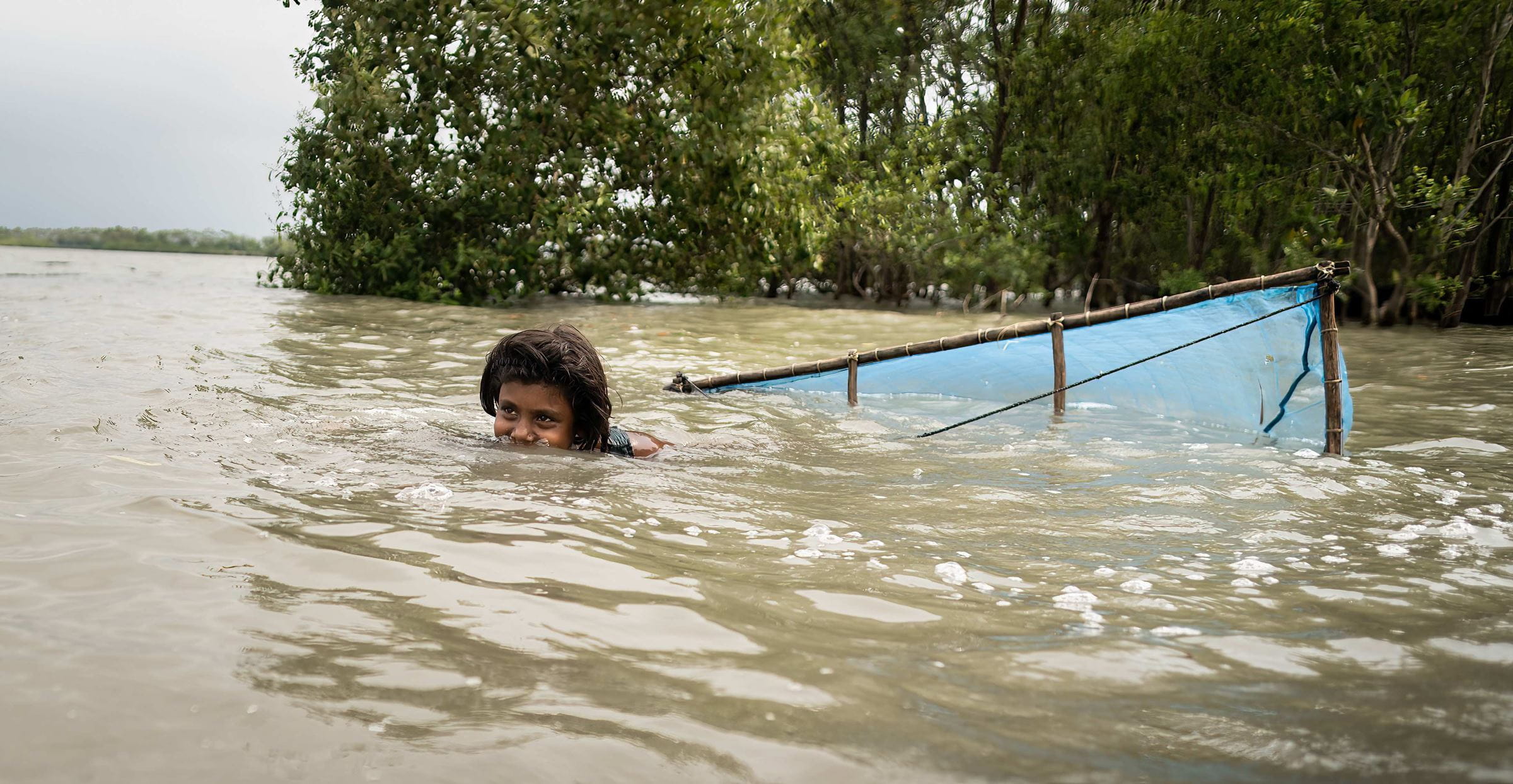 Bangladesch: Ein Mädchen schwimmt im Wasser und fischt Shrimps (Quelle: Lars Heidrich)