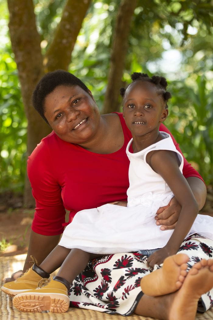Ein Mädchen aus Malawi sitzt im Schatten eines Baums auf dem Schoß ihrer Mutter. Beide lächeln in die Kamera (Quelle: Christian Nusch) Ein Mädchen aus Malawi sitzt im Schatten eines Baums auf dem Schoß ihrer Mutter. Beide lächeln in die Kamera (Quelle: Christian Nusch)