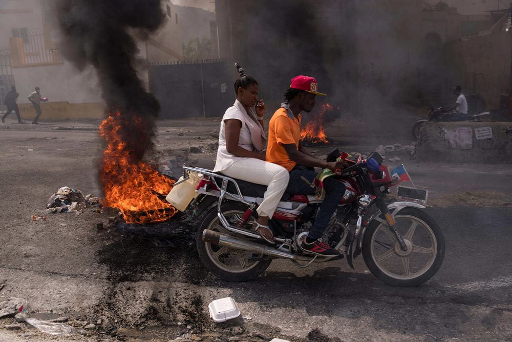 Eine Frau und ein Mann auf einem Motorrad passiert brennende Barrikaden (Quelle:IMAGO)