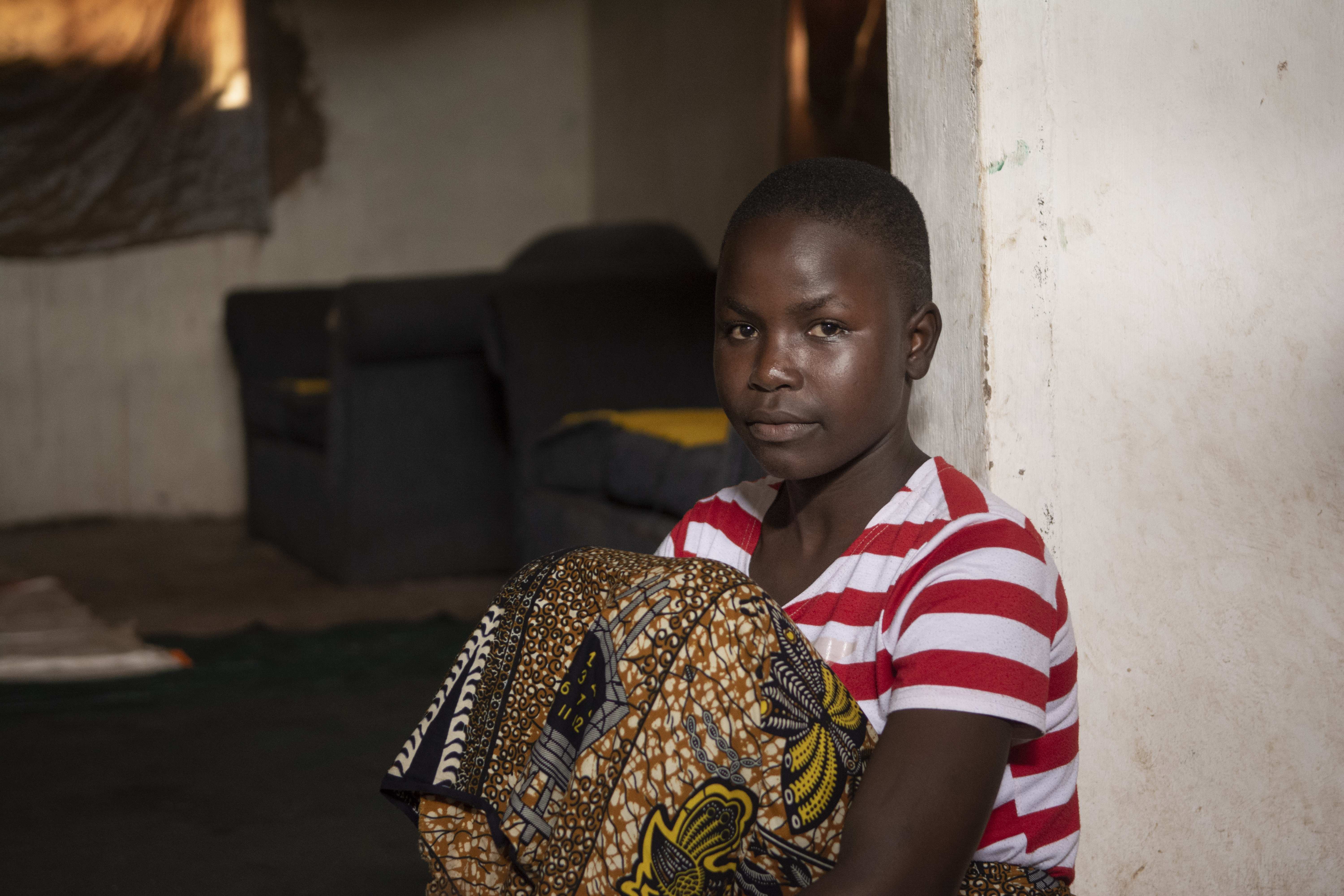 Ein Mädchen aus Malawi sitzt an einen Türrahmen gelehnt im Hauseingang und schaut ernst in die Kamera (Quelle: Christian Nusch)