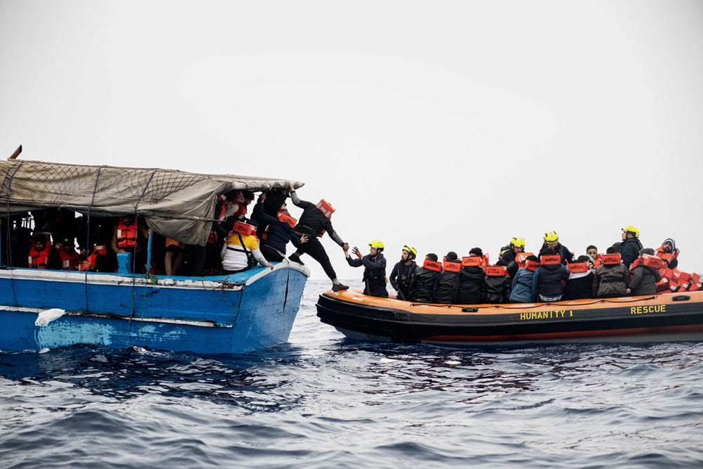 Von einem Flüchtlingsboot steigt jemand um in ein Rettungsboot (Quelle: Max Hirzel/SOS Humanity)