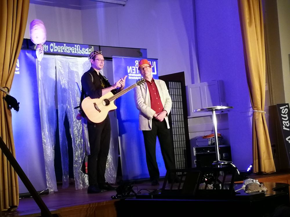 Ein Gitarrist und ein Mann mit rotem Stahlhelm auf einer Bühne (Quelle: Freundeskreis Düsseldorf)