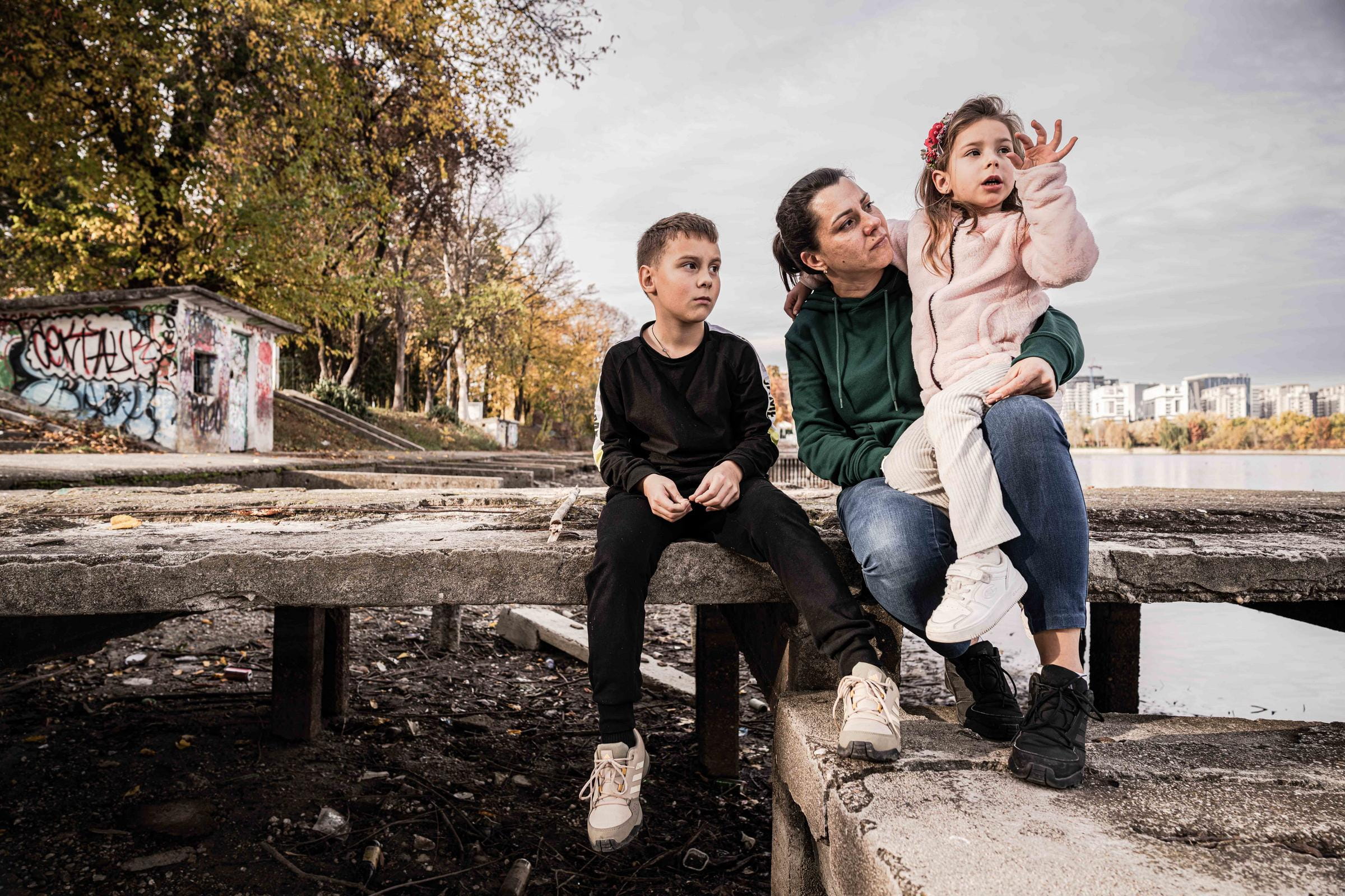 Mutter sitzt mit zwei Kindern draußen am Fluss (Foto: Jakob Studnar / Kindernothilfe)