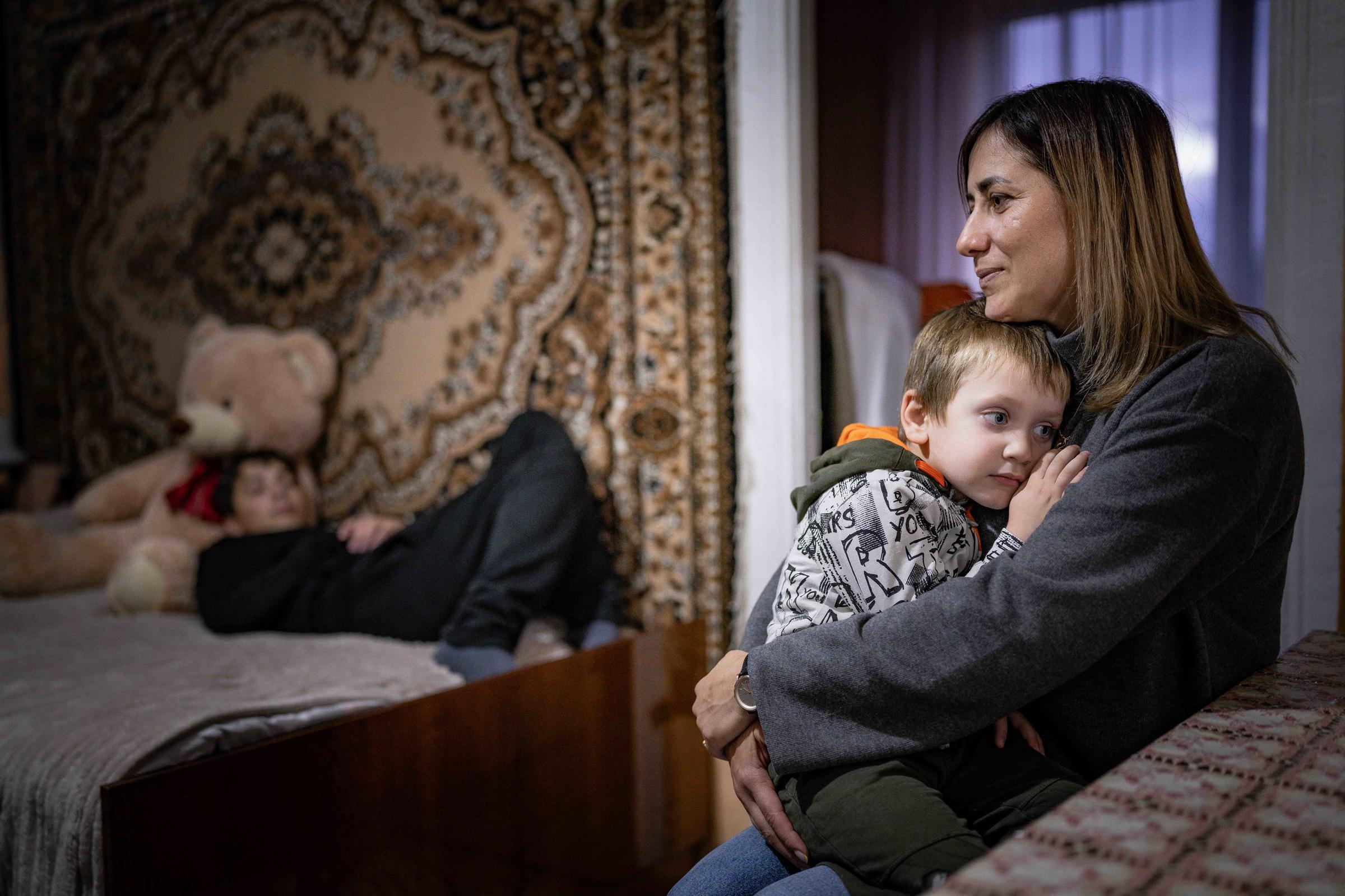 Eine Mutter hält einen Sohn im Arm, ein anderer Sohn liegt auf dem Bett (Quelle: Jakob Studnar)
