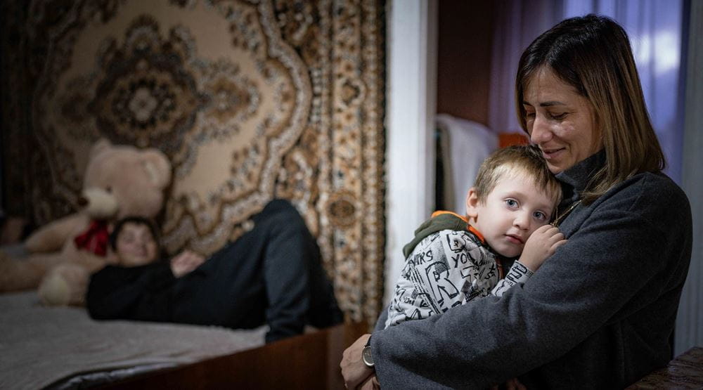 Eine Mutter hält einen Jungen im Arm, ein anderer liegt auf einem Bett (Quelle: Jaob Studnar) Eine Mutter hält einen Jungen im Arm, ein anderer liegt auf einem Bett (Quelle: Jaob Studnar)
