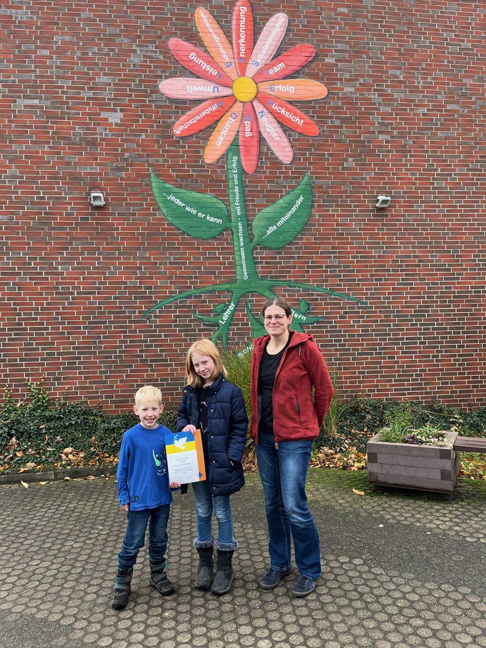 Ein Junge, ein Mädchen und eine Lehrerin stehen vor einer Mauer (Quelle: privat) Ein Junge, ein Mädchen und eine Lehrerin stehen vor einer Mauer (Quelle: privat)