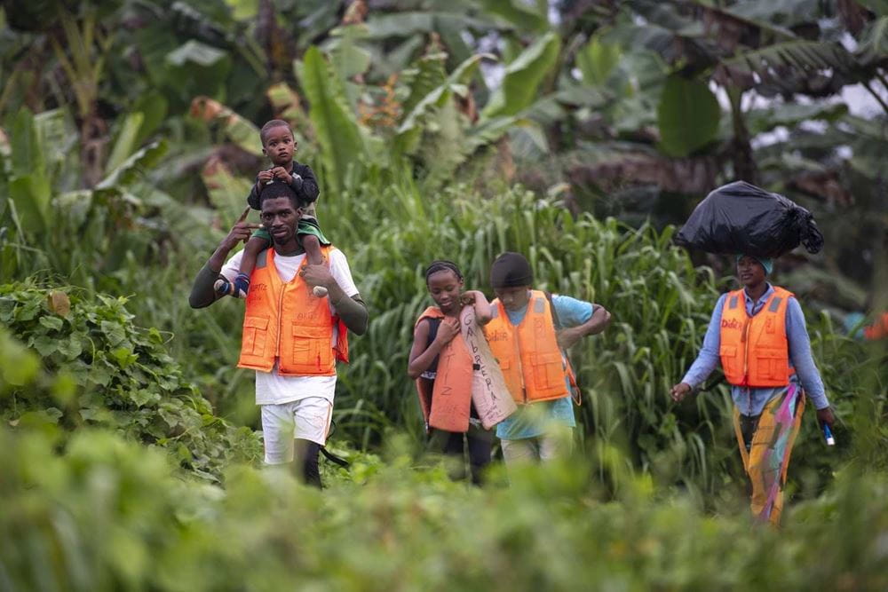 Vier Leute mit orange-farbenen Westen gehen durch einen Urwald, einer trägt ein Kind auf den Schultern (Quelle: Floran Kopp) Vier Leute mit orange-farbenen Westen gehen durch einen Urwald, einer trägt ein Kind auf den Schultern (Quelle: Floran Kopp)