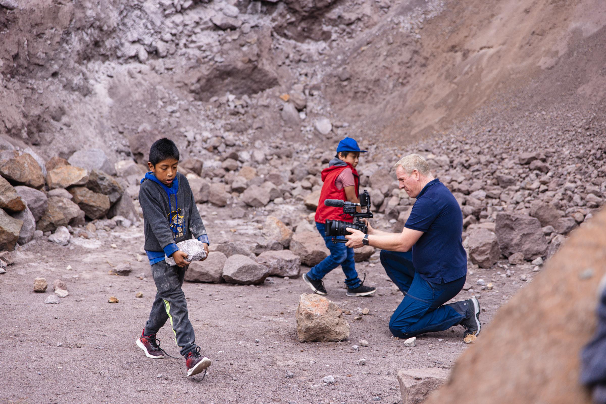 Ein Kameramann filmt zwei Kinder, die in einem Steinbruch Steine schleppen (Quelle: Martin Bondzio)