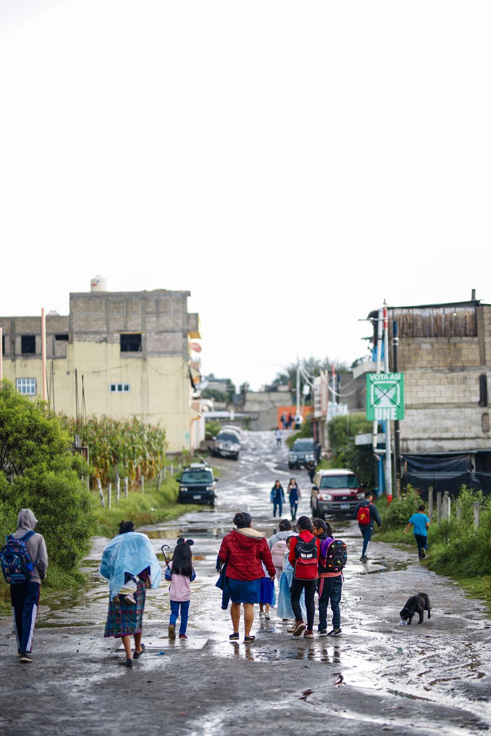Fußgänger, darunter Schulkinder, gehen eine nasse Straße entlang (Quelle: Martin Bondzio)