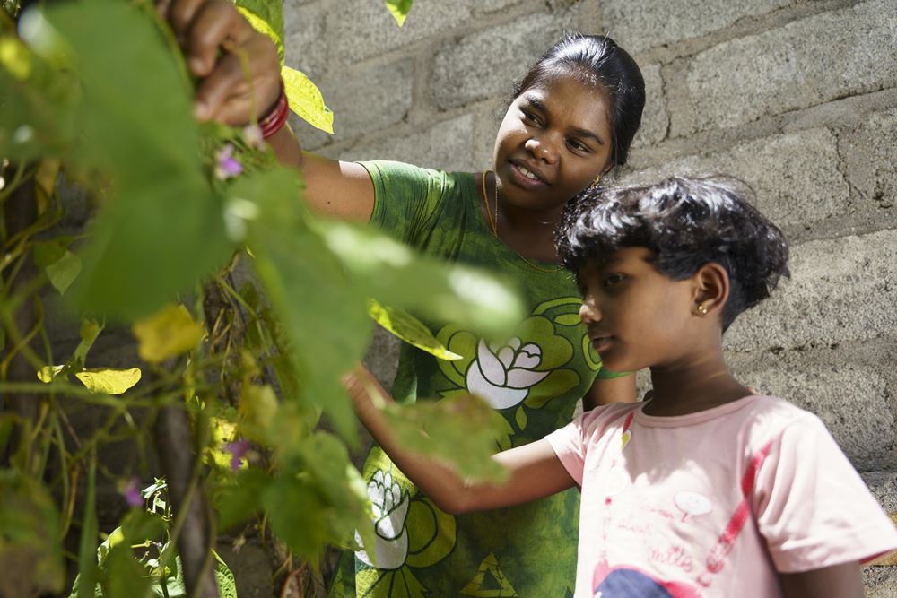 Eine Frau zeigt ihrer Tochter eine Stangenbohnenpflanze (Quelle: Christian Nusch)