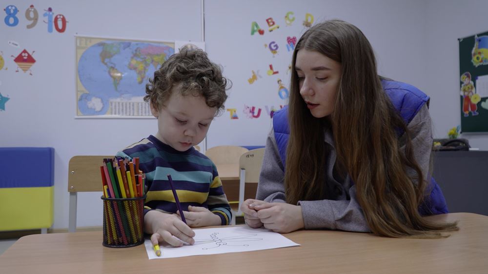 Kind malt in Begleitung von Lehrpersonal. Die Kindernothilfe und ihre Partner unterstützen Kinder mit ergänzenden Bildungsangeboten und psychosozialer Hilfe (Foto: Myrne Nebo – Peaceful Heavens of Kharkiv) Kind malt in Begleitung von Lehrpersonal. Die Kindernothilfe und ihre Partner unterstützen Kinder mit ergänzenden Bildungsangeboten und psychosozialer Hilfe (Foto: Myrne Nebo – Peaceful Heavens of Kharkiv)