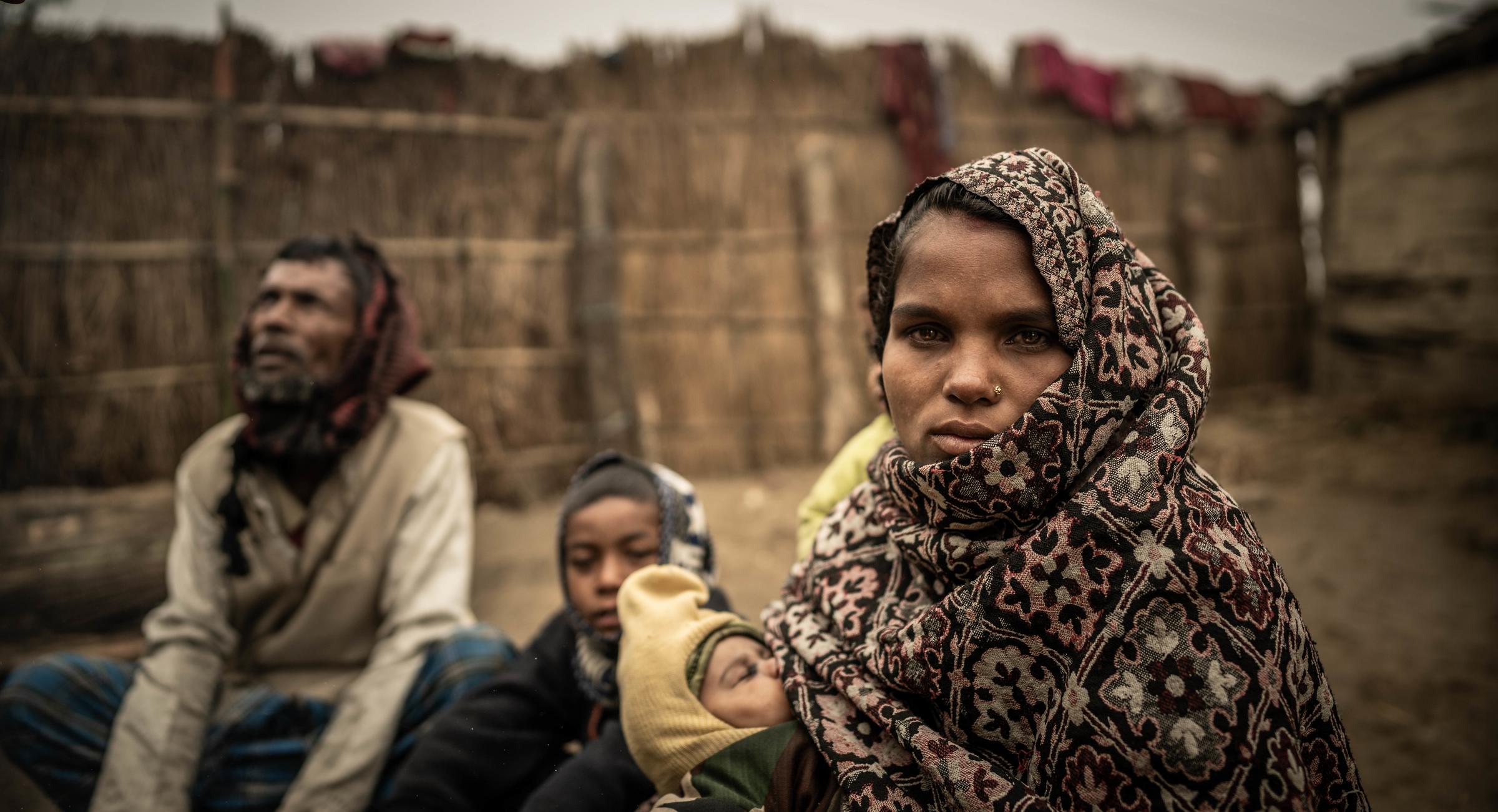 Eine junge Frau mit ihrem Baby auf dem Arm sitzt in ihrem Dorf auf dem Boden. (Quelle: Jakob Studnar)