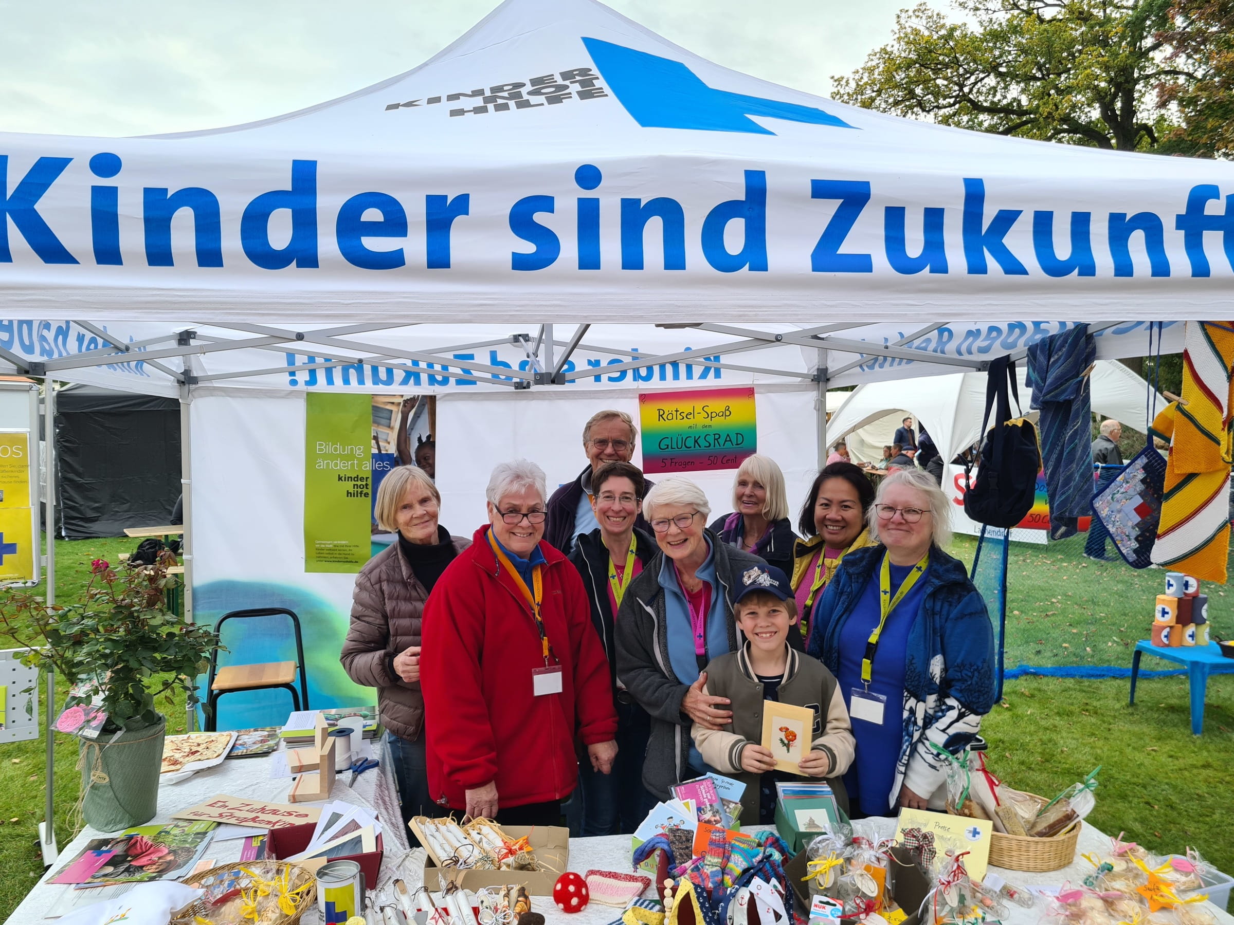 Ein Arbeitskreis mit einem kleinen Jungen in der Mitte steht in einem Kindernothilfe-Pavillon (Quelle: Christopher Vent)