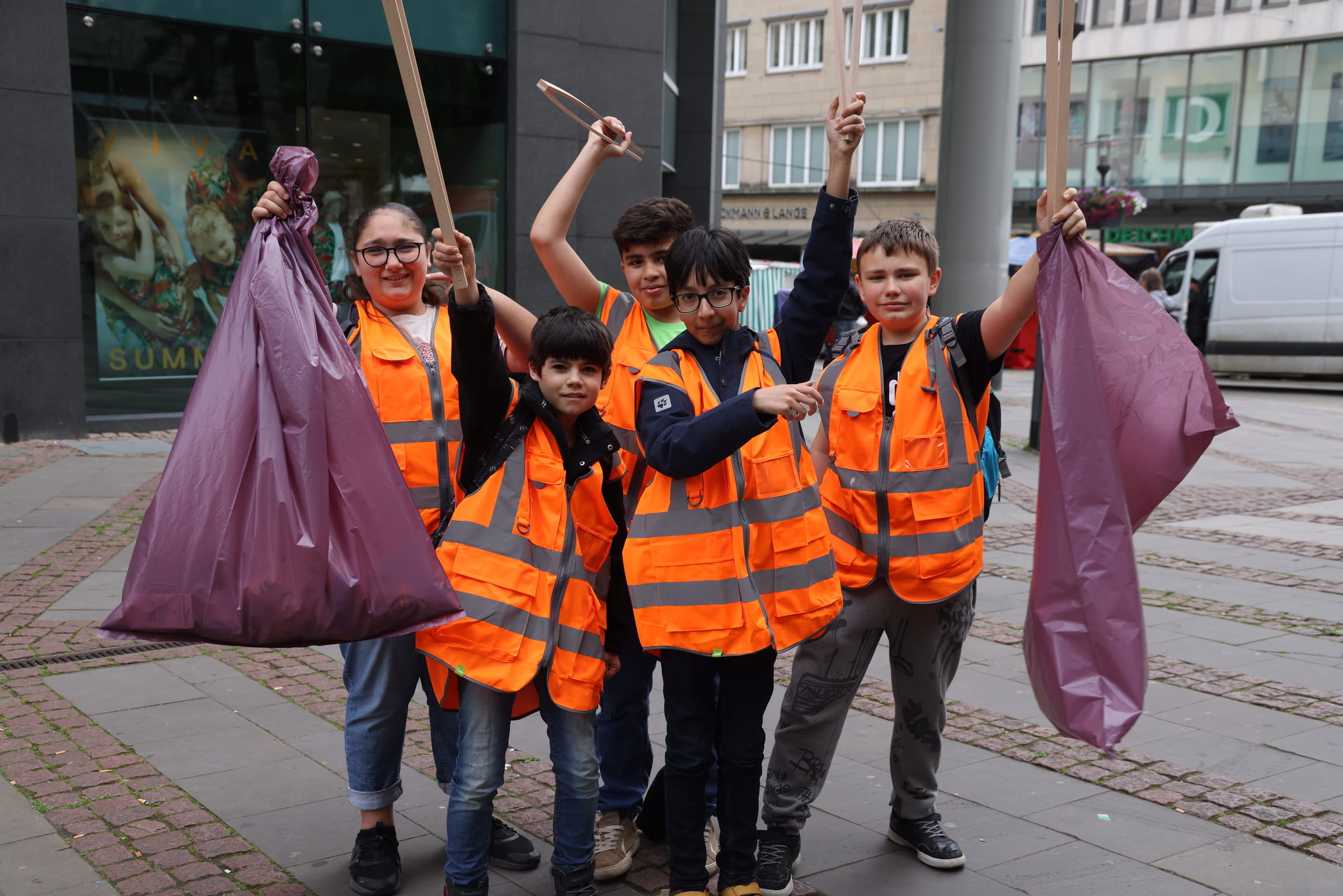 Mädchen und Jungen tragen Warnwesten und Müllbeutel und lächeln in die Kamera (Quelle: Ludwig Grunewald)