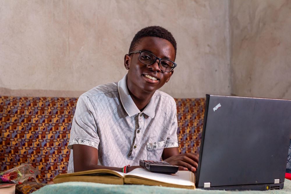 Junge sitzt am Laptop und lächelt in die Kamera (Quelle: Kindernothilfe) Junge sitzt am Laptop und lächelt in die Kamera (Quelle: Kindernothilfe)