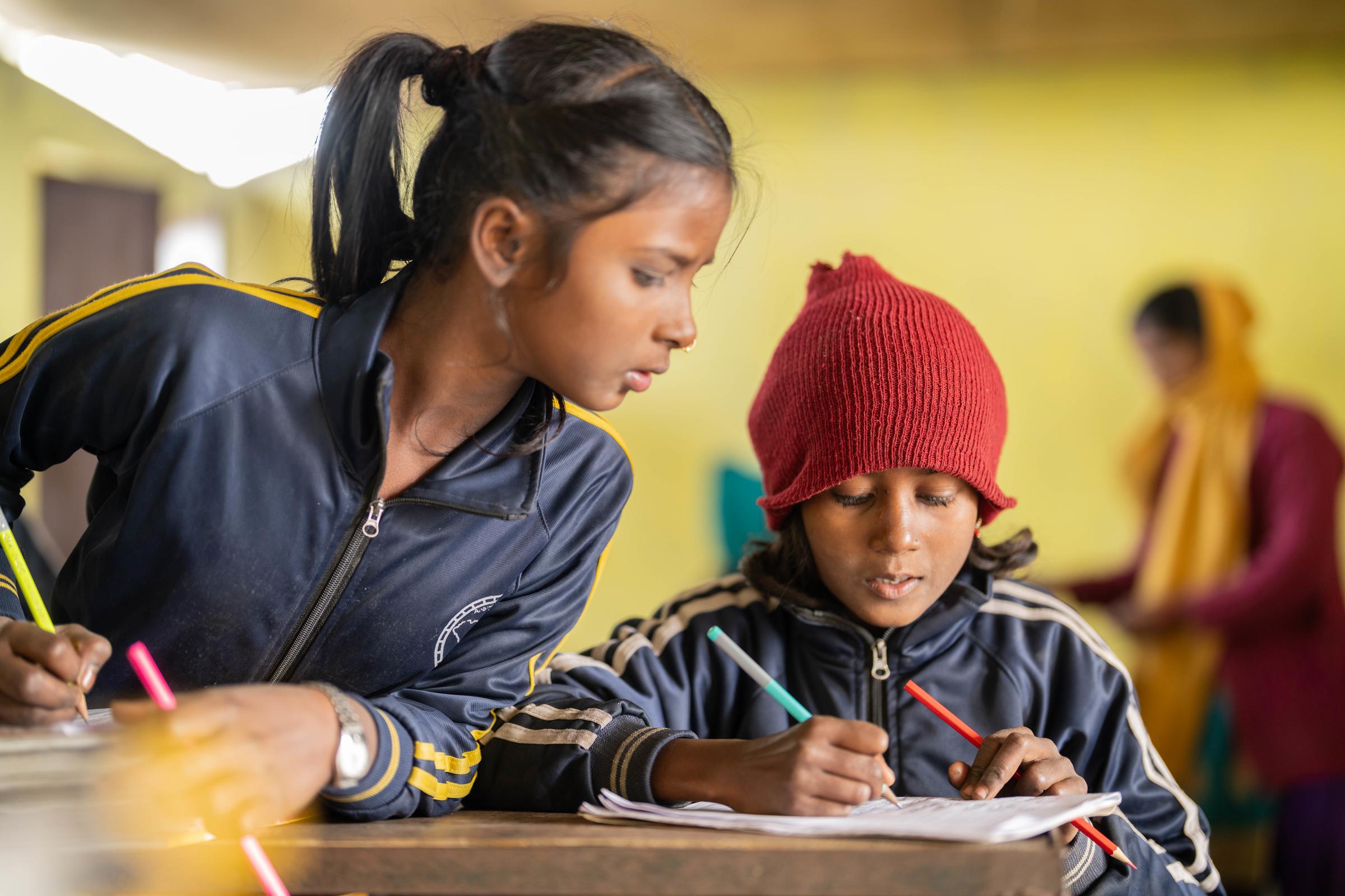 Zwei Mädchen sitzen am Tisch und schreiben. Ein Mädchen schaut bei dem anderen ab (Quelle: Jakob Studnar)