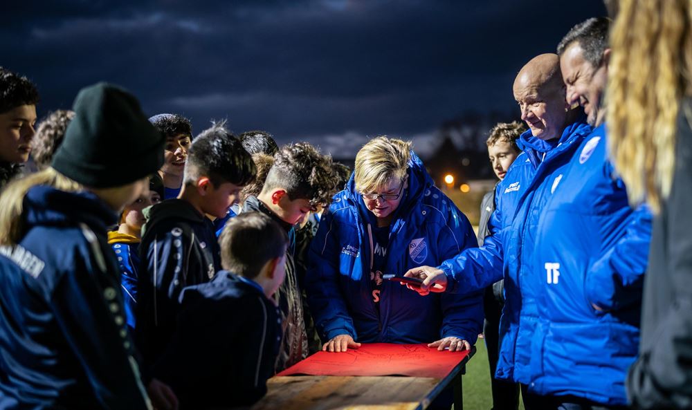 Kinder und Trainer*innen stehen beim Partizipationstag, der zum Prozess des Schutzkonzeptes dazu gehört, auf einem Fußballplatz um einen Tisch herum und schauen auf ein rotes Plakat (Foto Jakob Studnar) Platzhalterbild