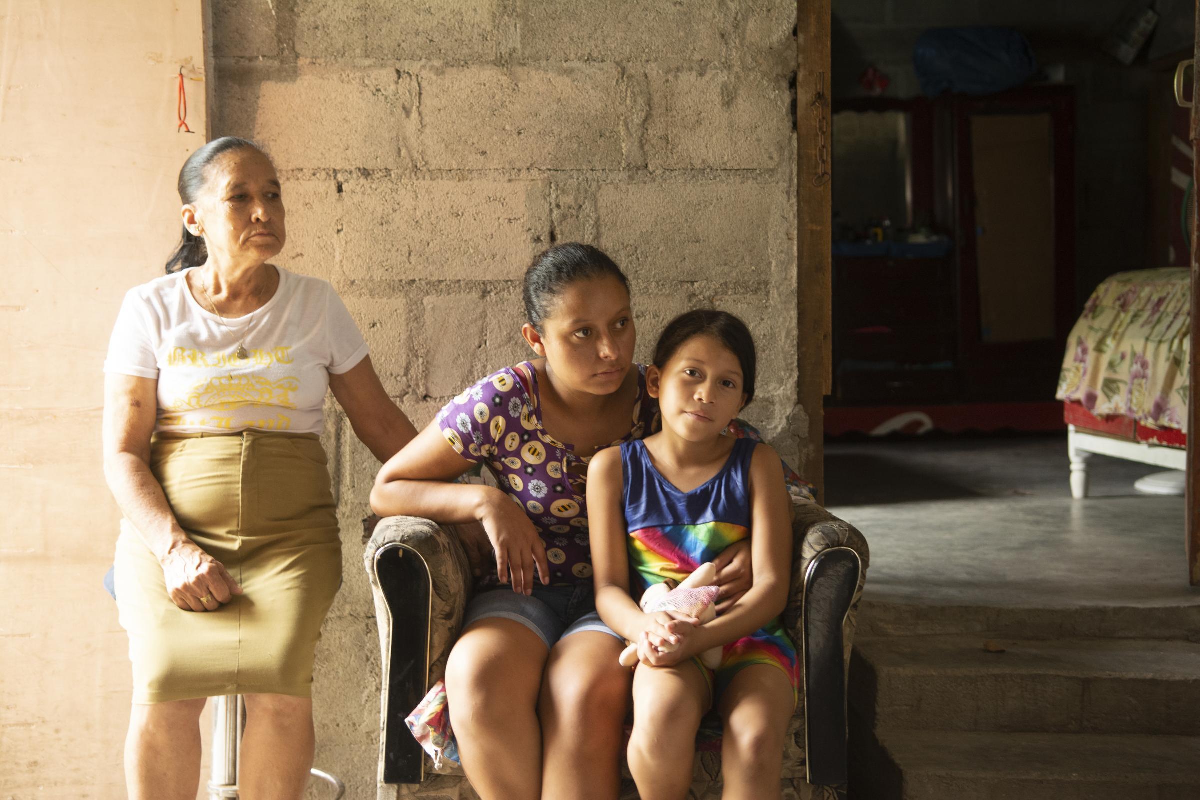 Eine Mutter sitzt mit ihrer Tochter gemeinsam auf einem Sessel in Bordos, Honduras. Die Grossmutter steht daneben (Quelle: Christian Nusch/Victor Zavaleta Carbajal)